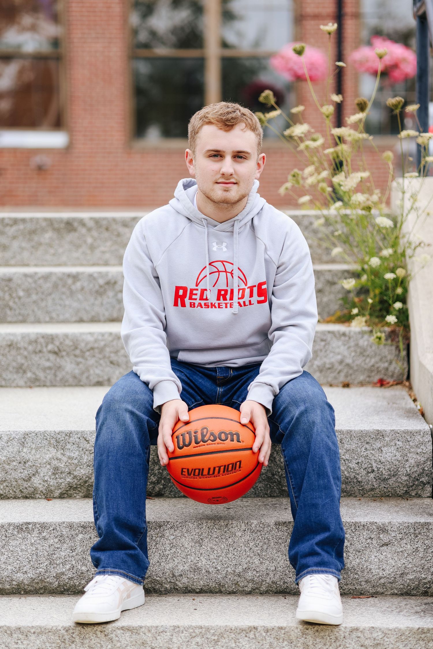 A person in a gray hoodie sits on concrete steps holding a basketball.
