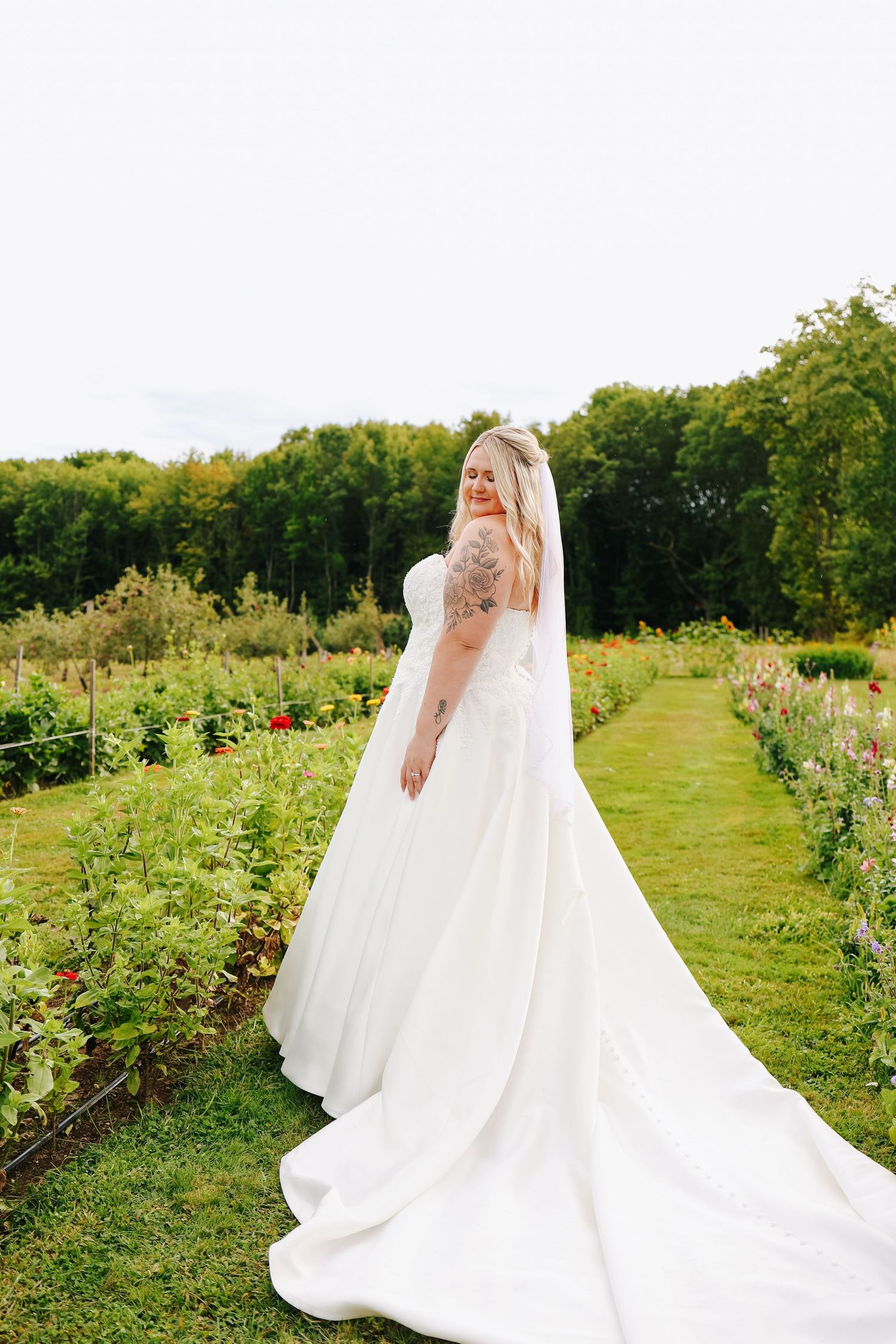 Bride with flowing white wedding dress train spread across a lush garden path.