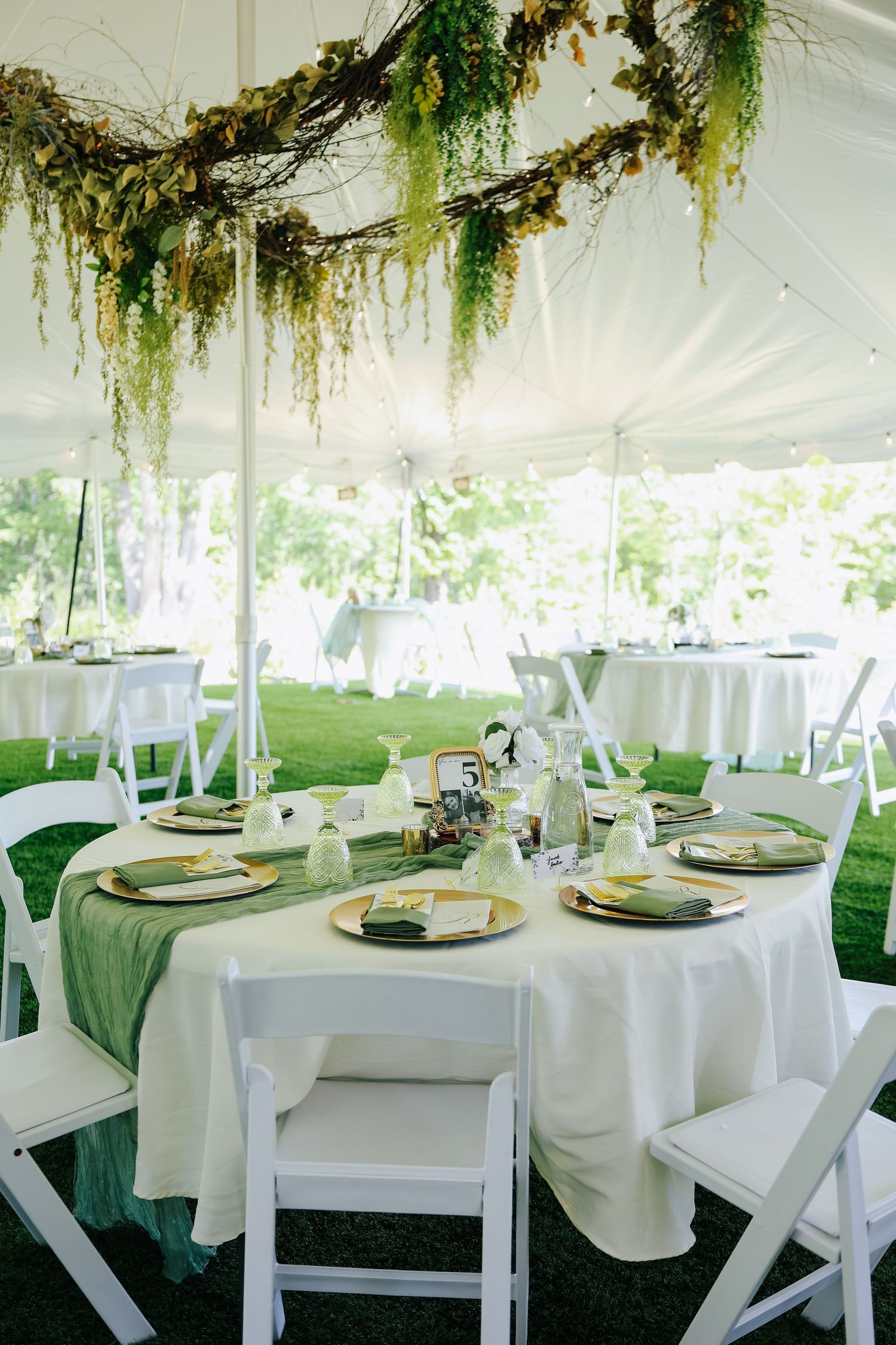 Wedding reception tables set under a tent with hanging greenery and white linens.