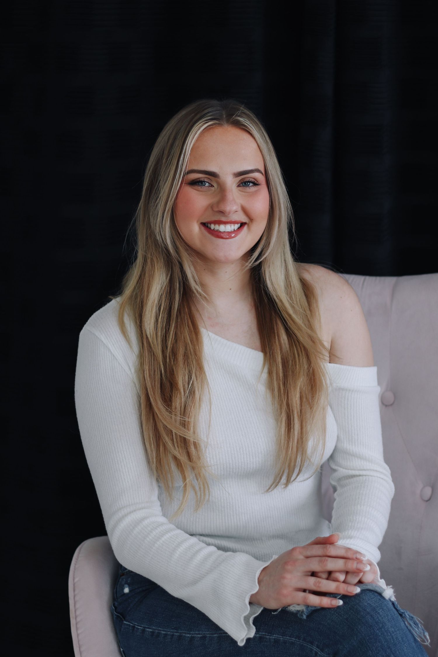 Person in white sweater and jeans poses casually against dark background in professional headshot series.