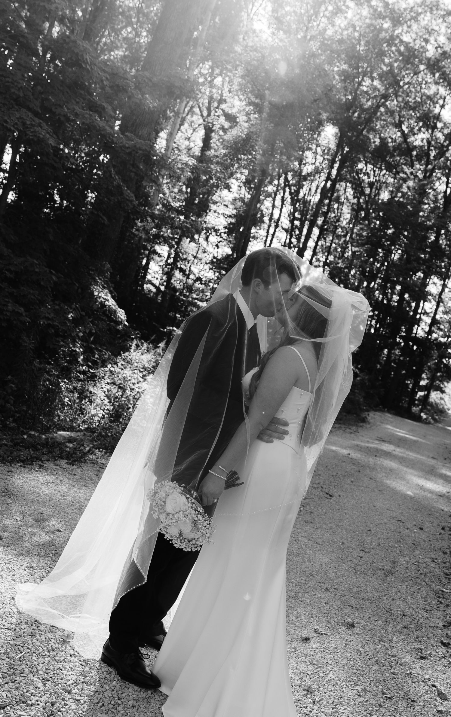 Black and white wedding photo showing couple embracing outdoors among trees.