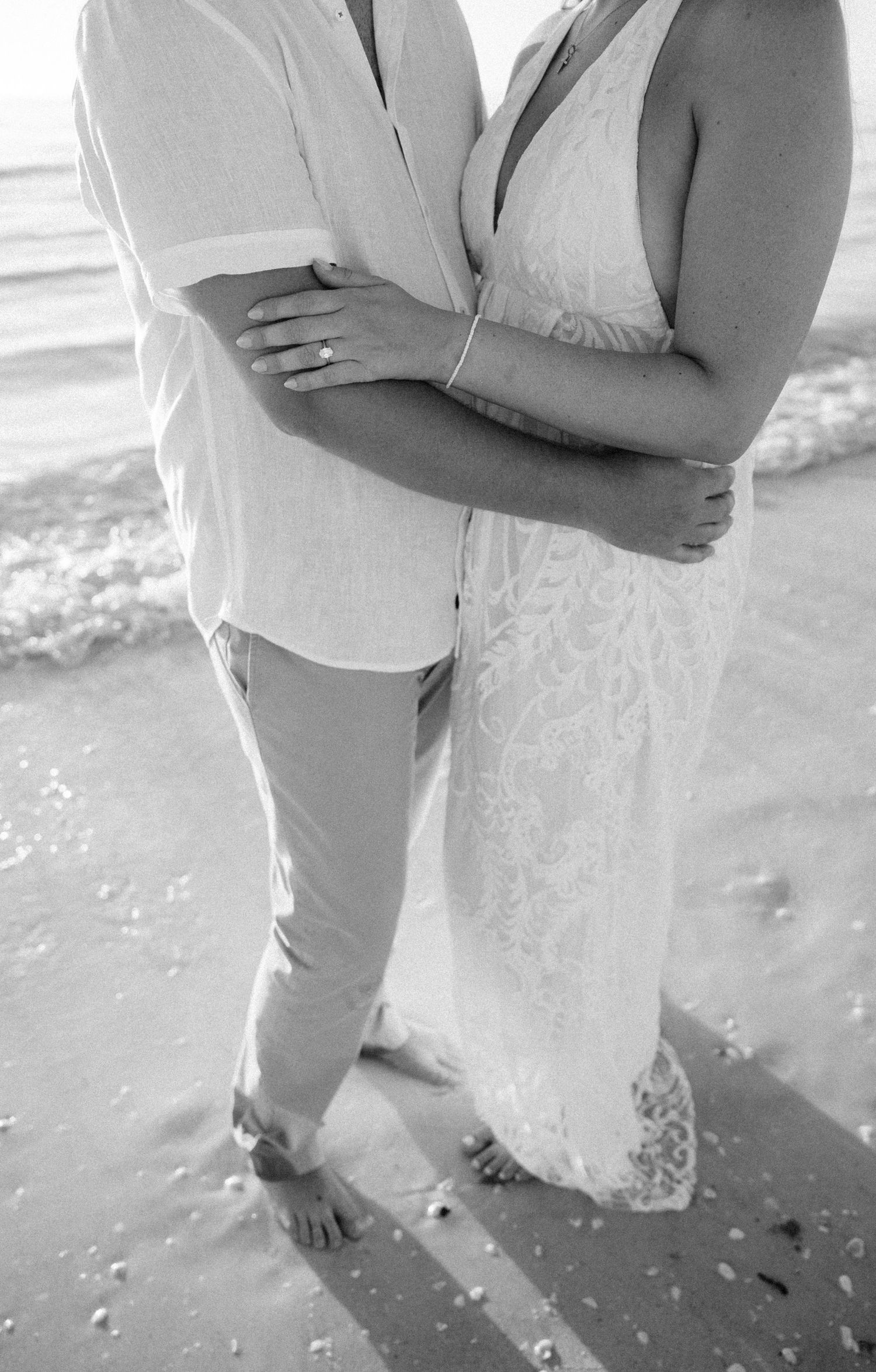 A romantic black and white photo series showing a couple embracing on a beach with bare feet in the sand.