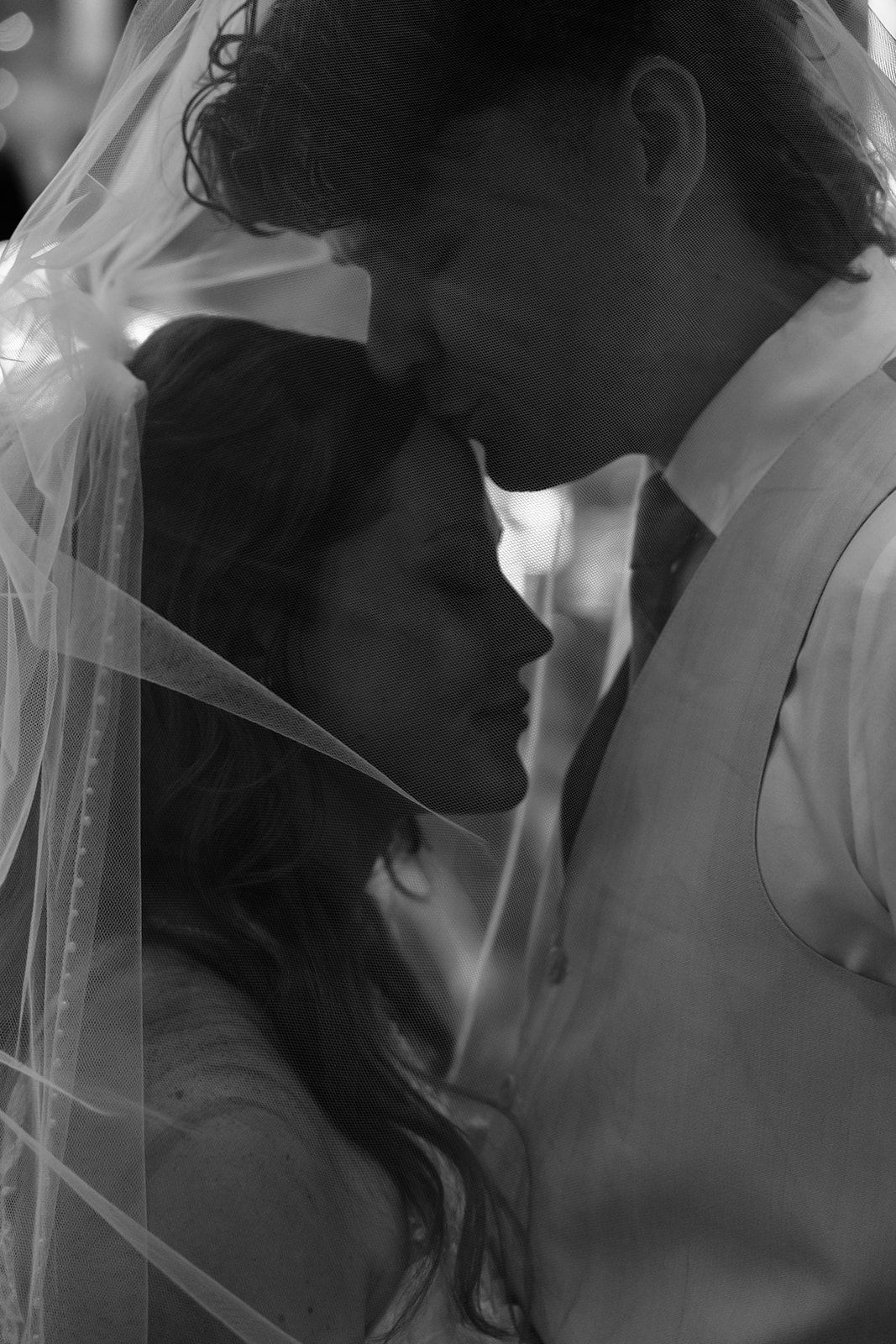 Black and white photo of bride and groom sharing an intimate moment under a wedding veil.