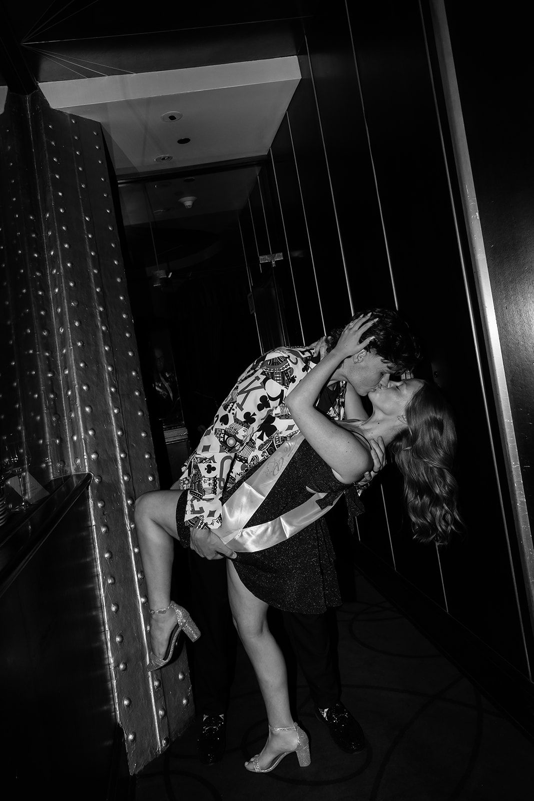Black and white photo of a couple sharing a romantic kiss in a dimly lit hallway.
