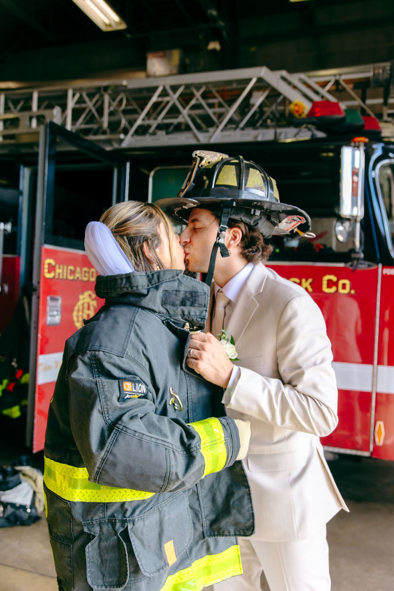 A couple shares a kiss in firefighter gear and a wedding suit in front of a Chicago fire truck.