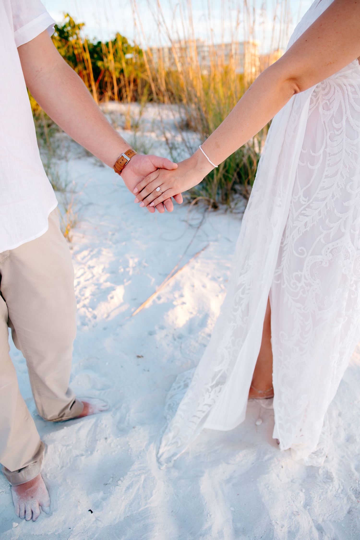 Bare feet and flowing white dress hem walking on pristine white sand beach at sunset.