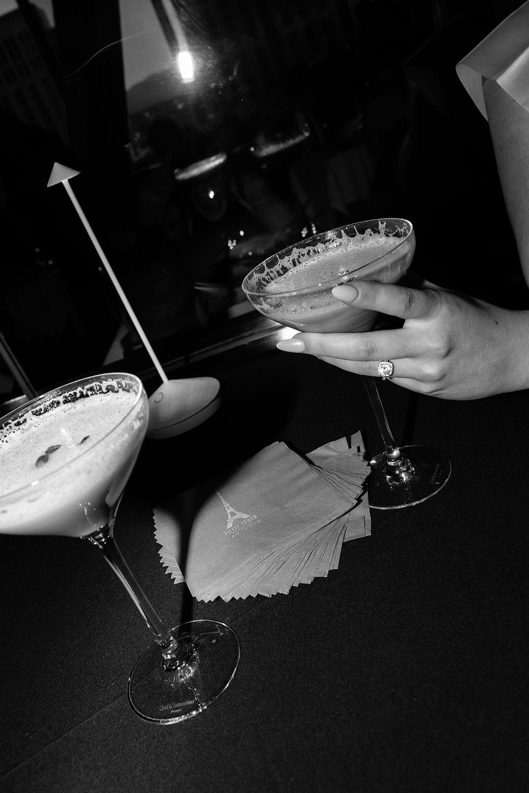Black and white photo of a woman holding a cocktail glass with a sugared rim at a bar.