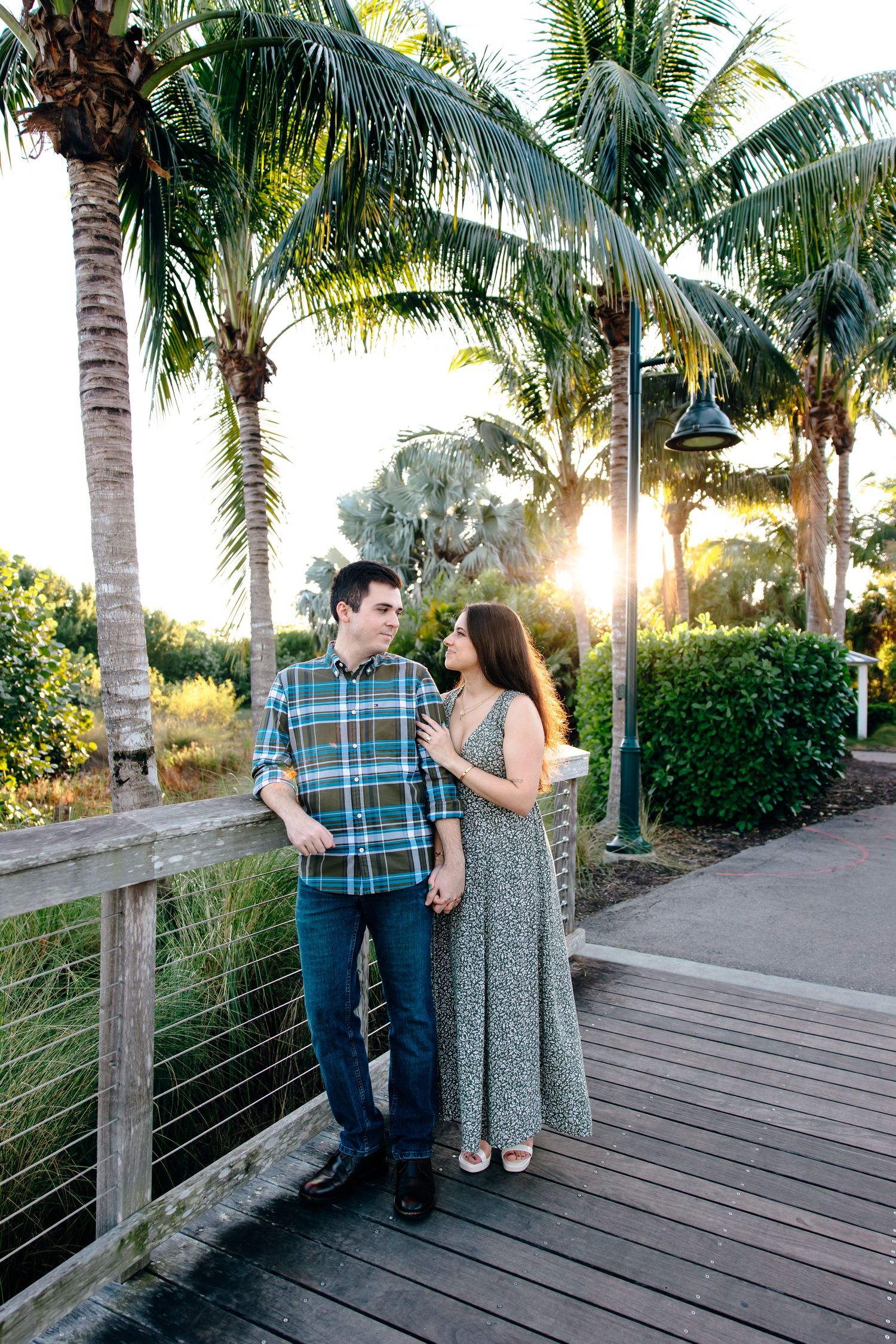 Couple holding hands on a wooden boardwalk surrounded by palm trees at golden hour sunset.