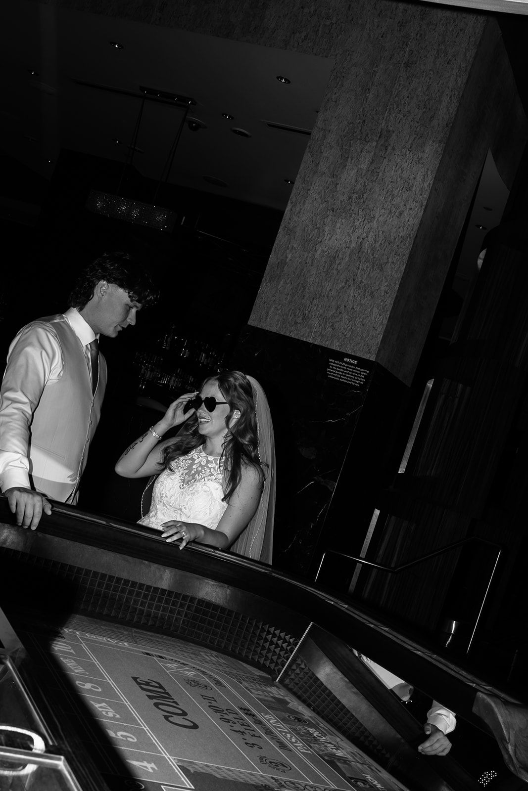 Bride in sunglasses and groom at casino craps table in black and white wedding photo.