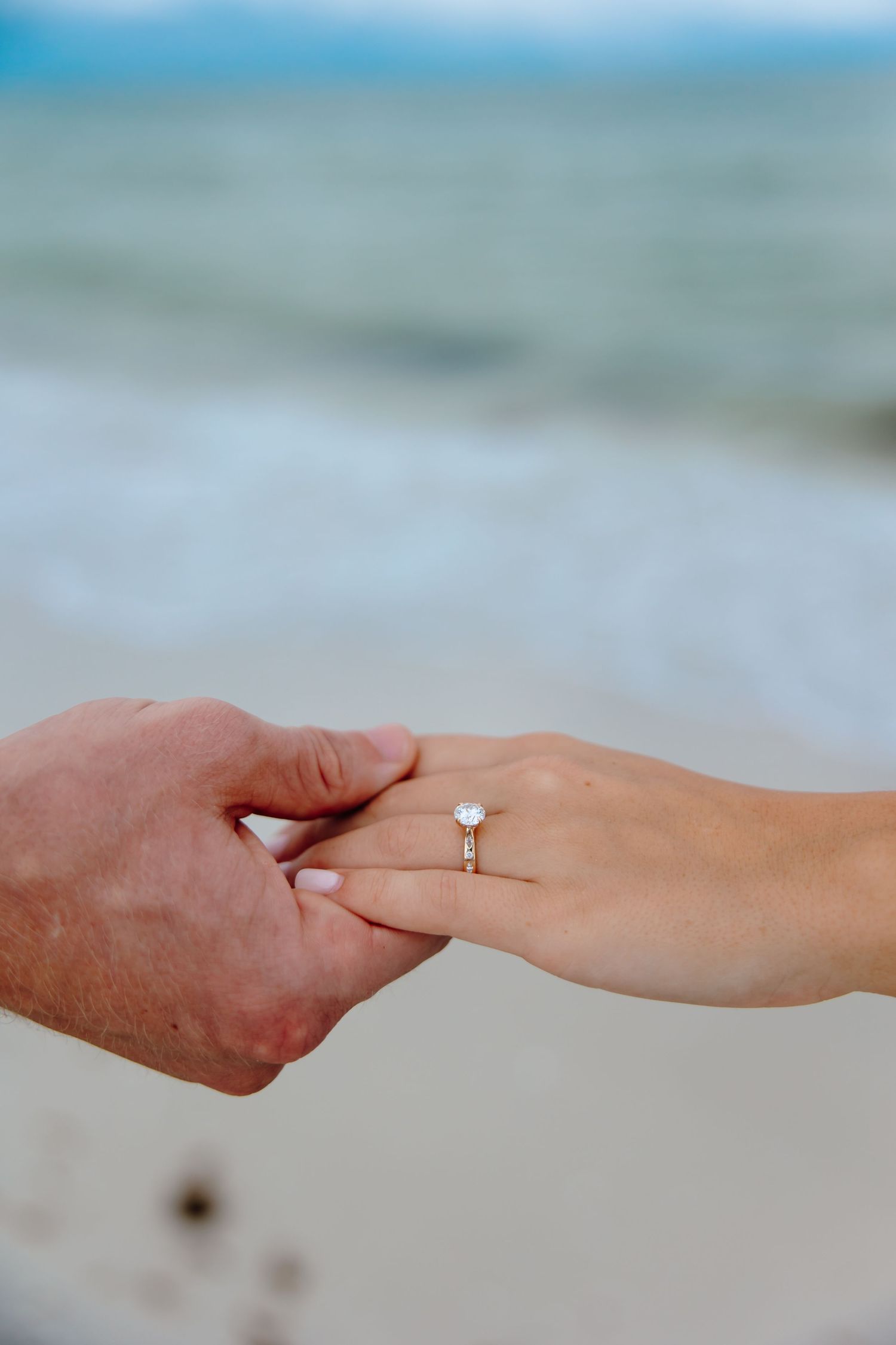 Close-up photo series showing hands exchanging an engagement ring on a beach with blurred ocean background.