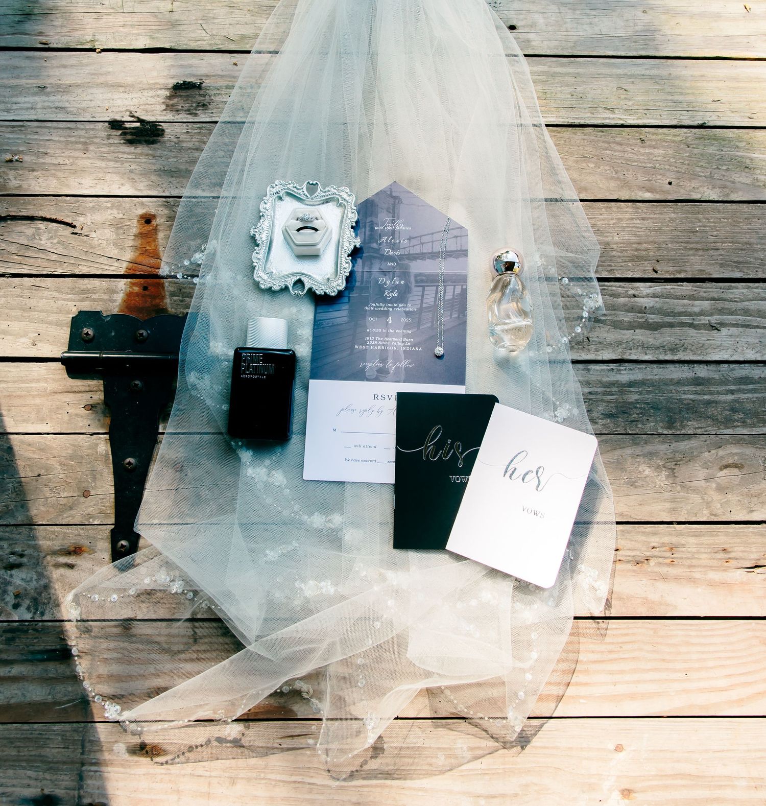 Wedding flat lay with veil, invitations, rings, and perfume on rustic wood deck.