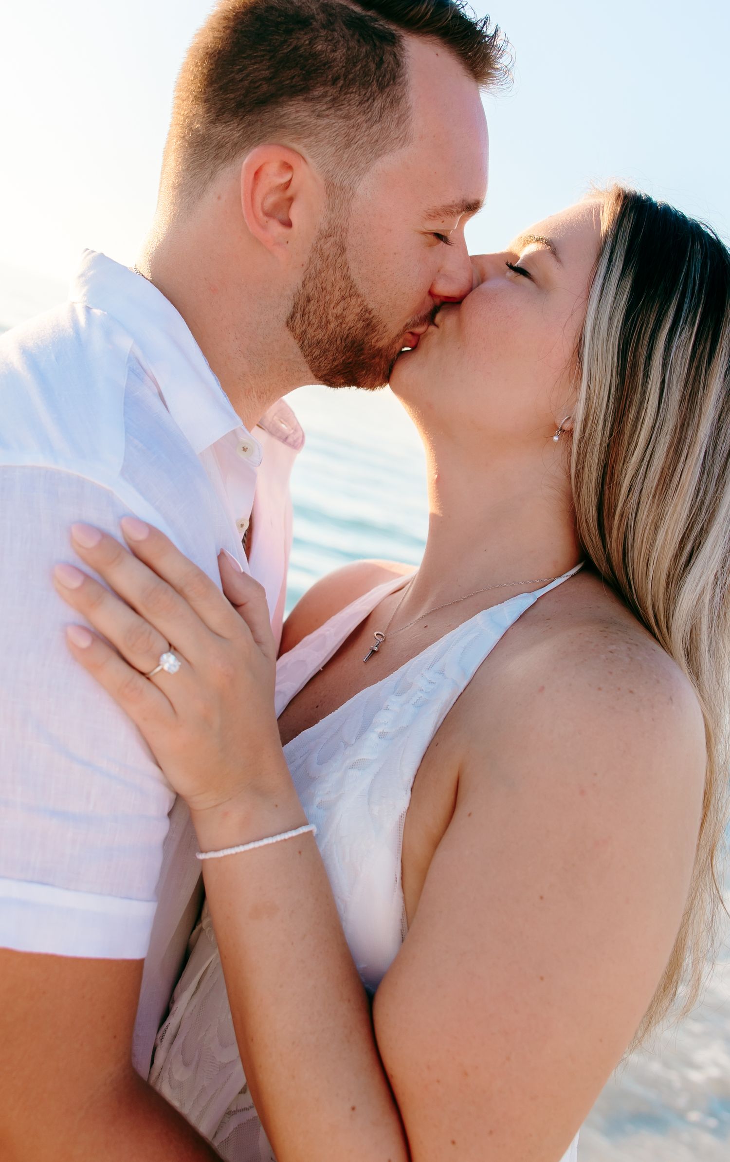 A romantic couple shares tender kisses on the beach during a sunset photoshoot.