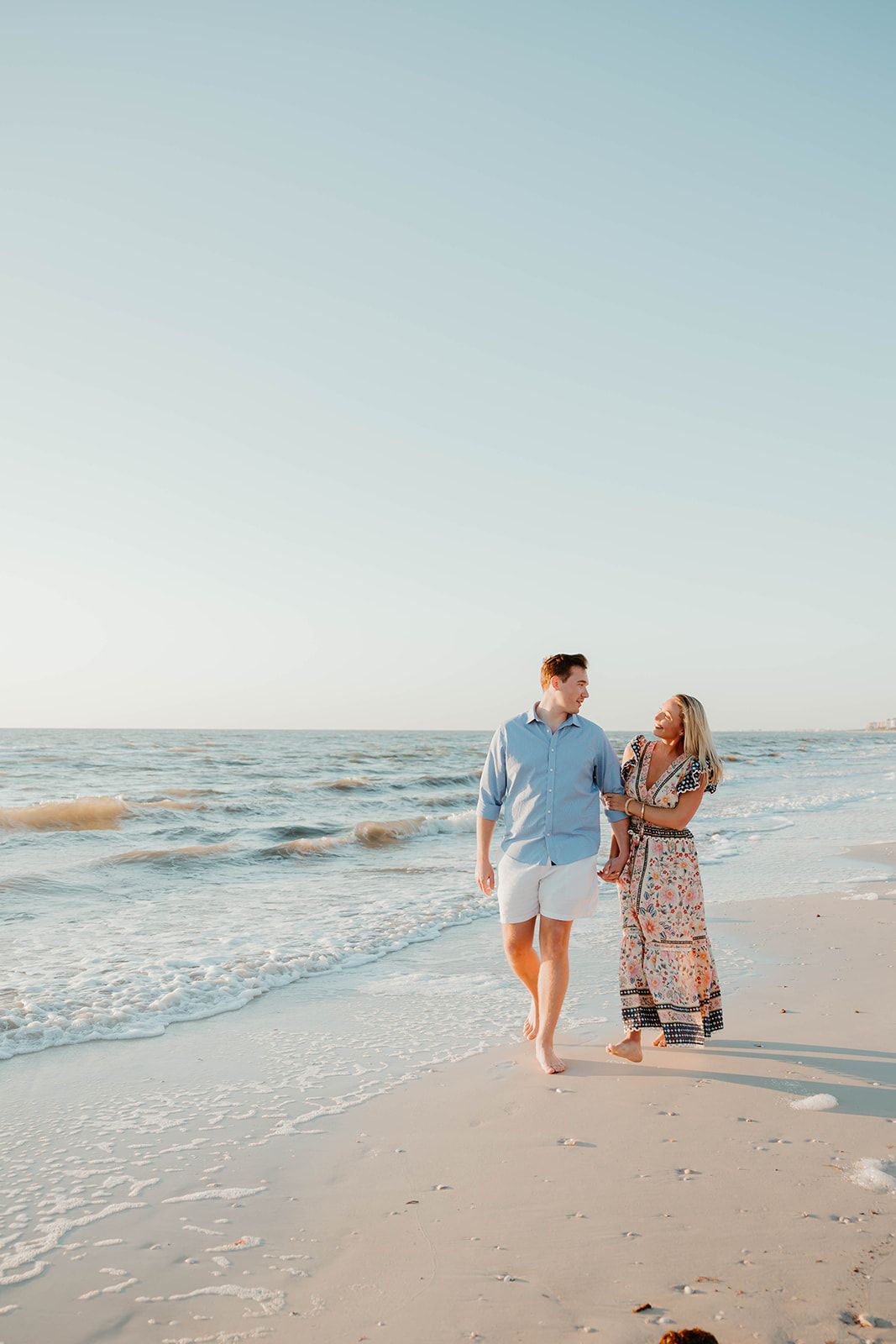 A couple walking along the shoreline during sunset after their beach proposal.