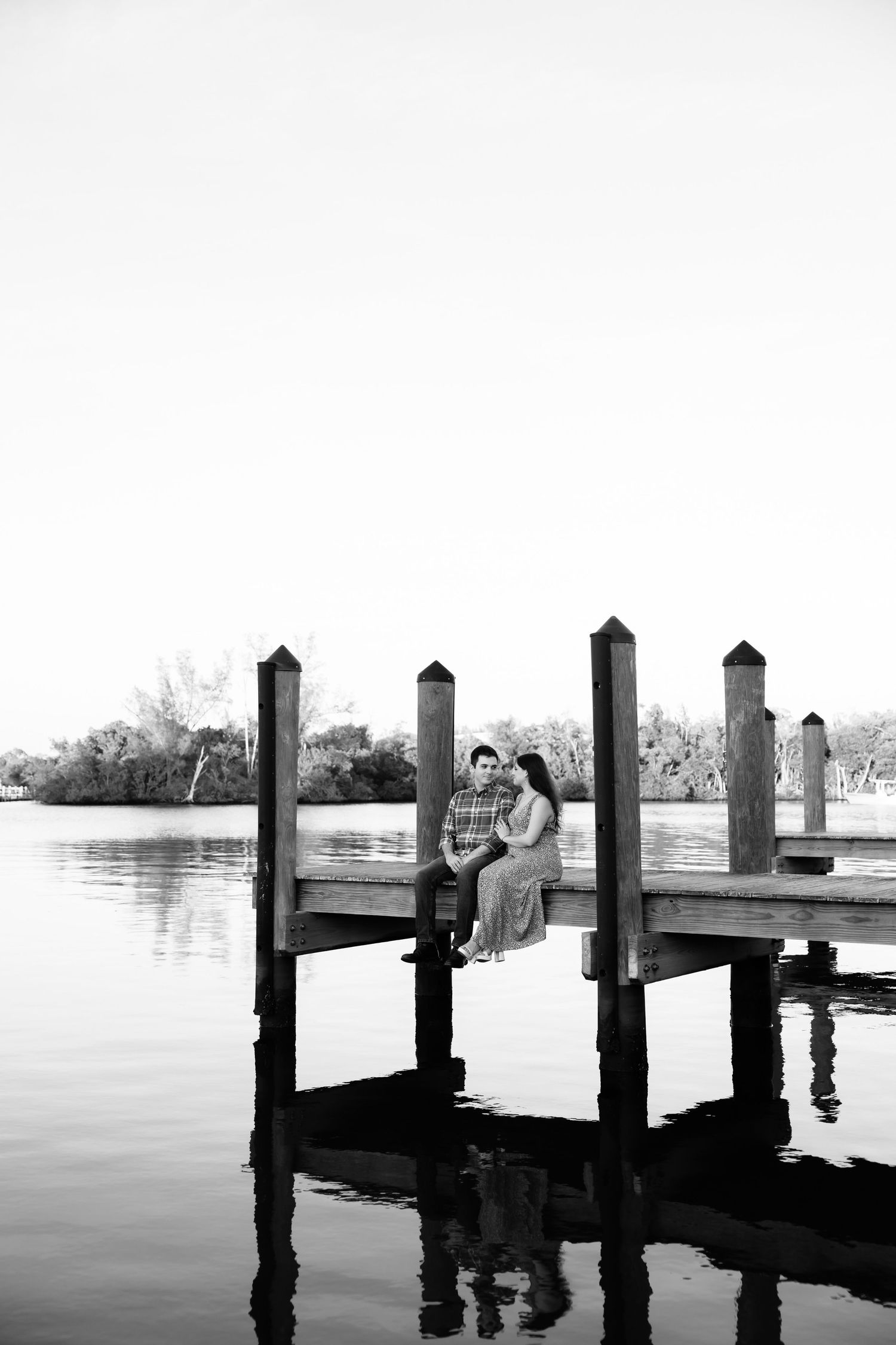 Couple sitting together on a wooden dock over calm water, black and white romantic outdoor portrait.