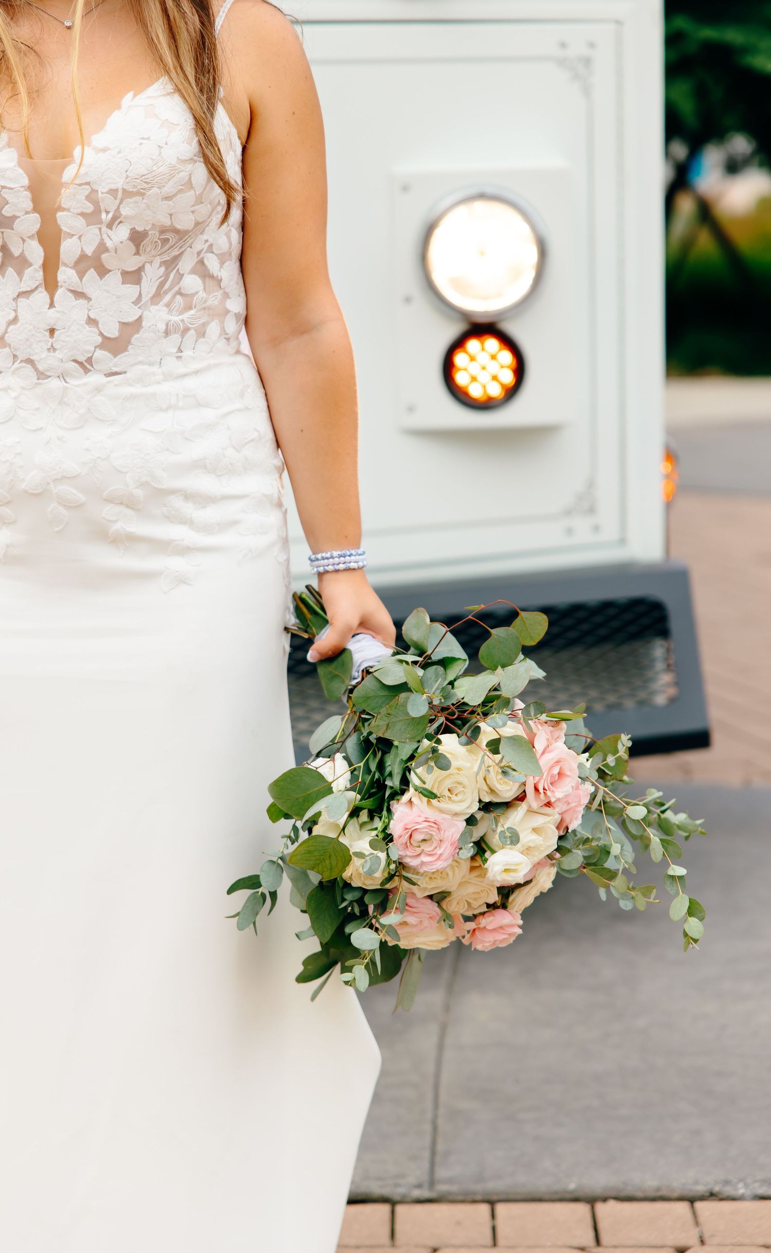 Close-up details of a bride in a white lace wedding dress holding a delicate pink and white floral bouquet with greenery.