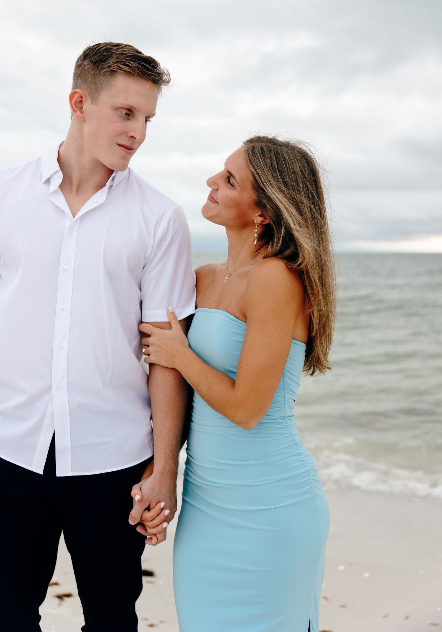 A couple in white shirt and blue dress share intimate moments on a cloudy beach.