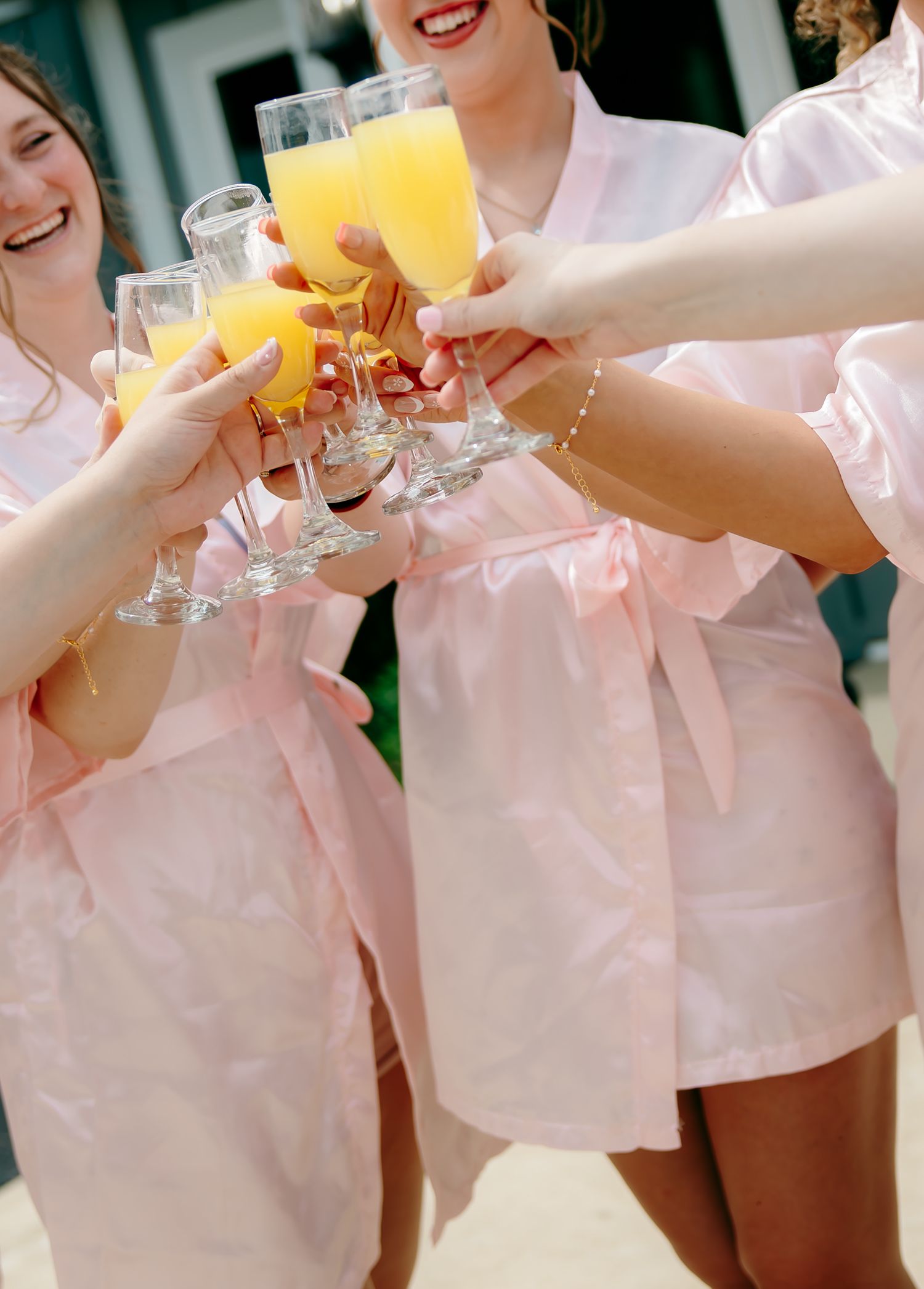 Bridesmaids in pink robes toasting with mimosas, raising champagne glasses filled with orange juice.
