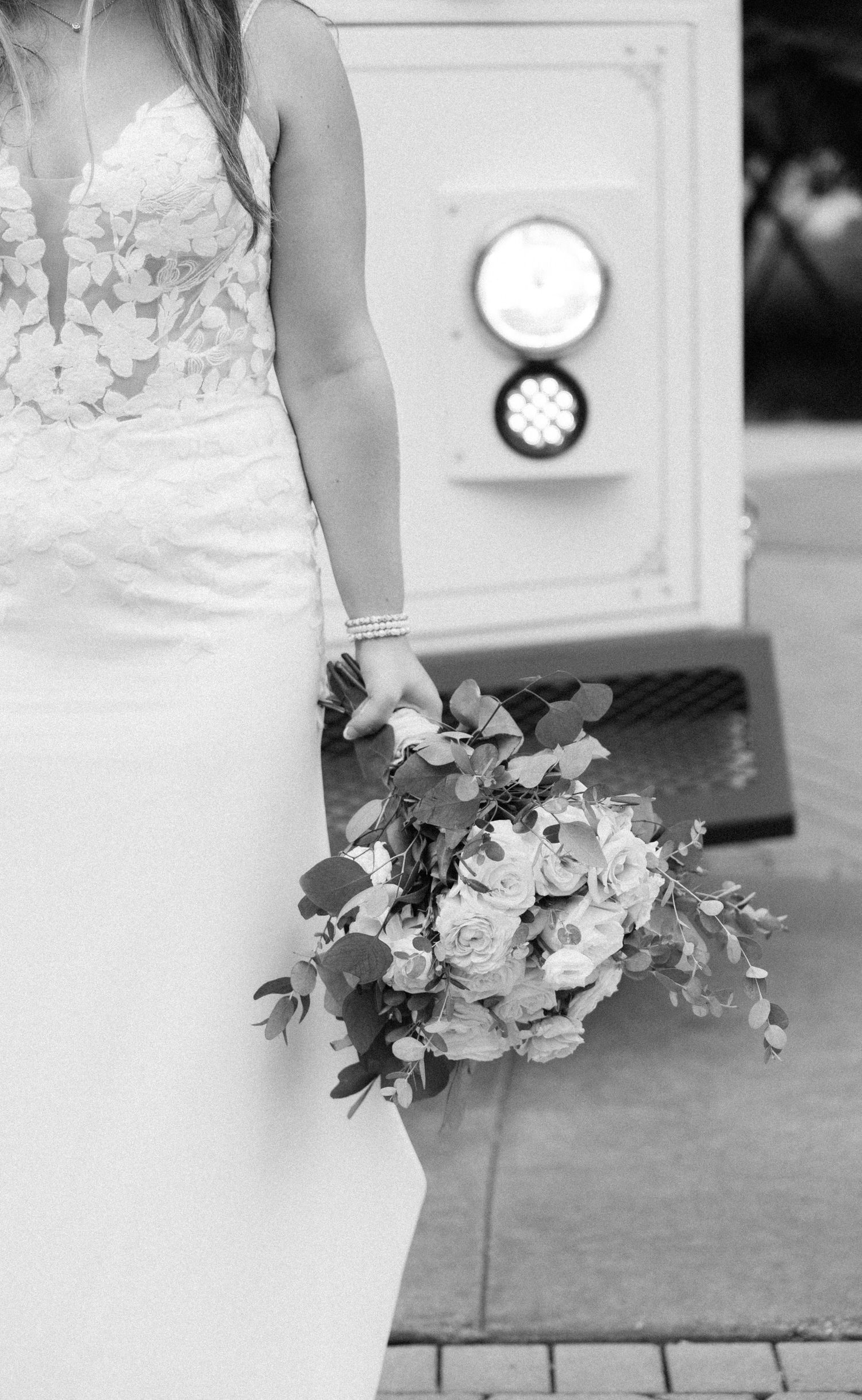 Black and white photo of a bride in a lace gown holding a bouquet of roses and eucalyptus.