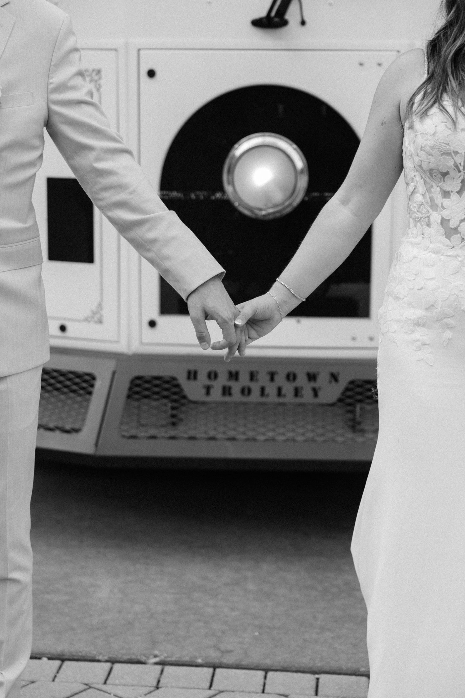 Black and white wedding photo showing hands holding a bouquet against formal white attire.