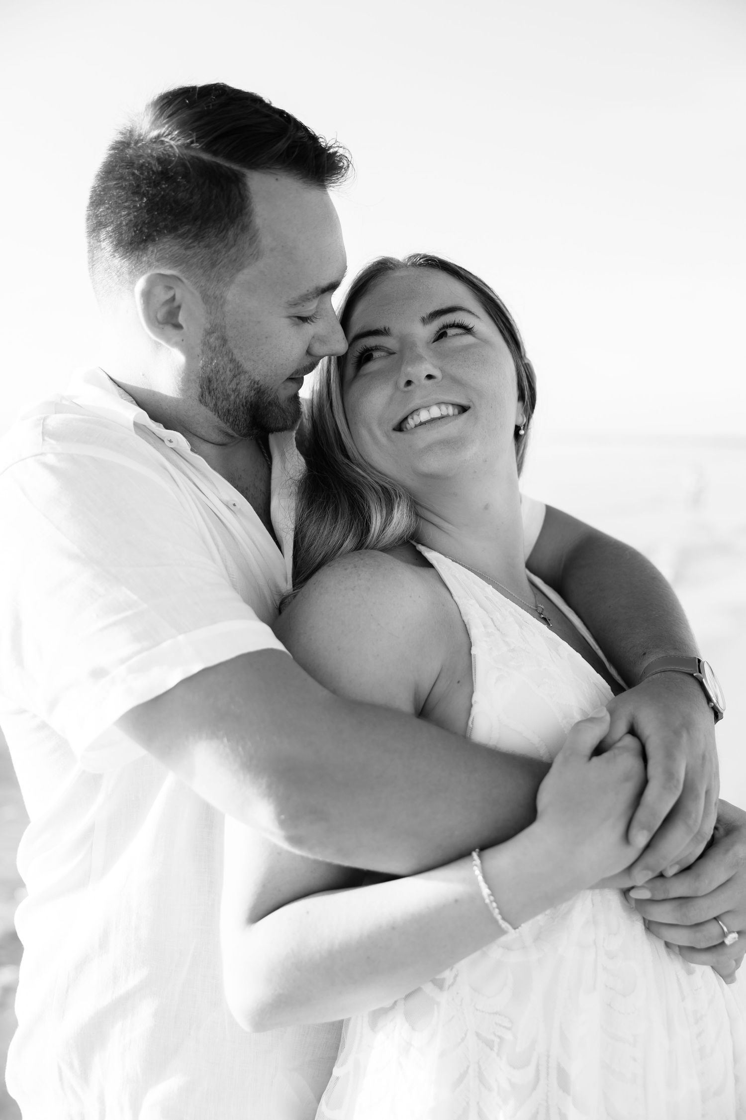 A romantic black and white portrait of a couple embracing and smiling together outdoors.