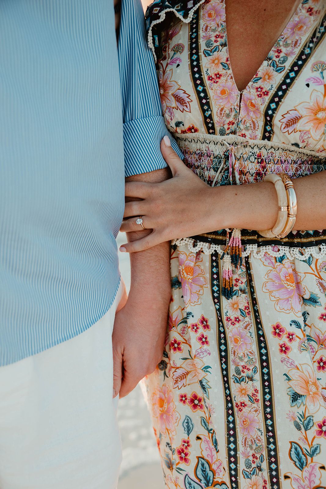 Close-up details of a floral dress and light blue shirt during a beach engagement.