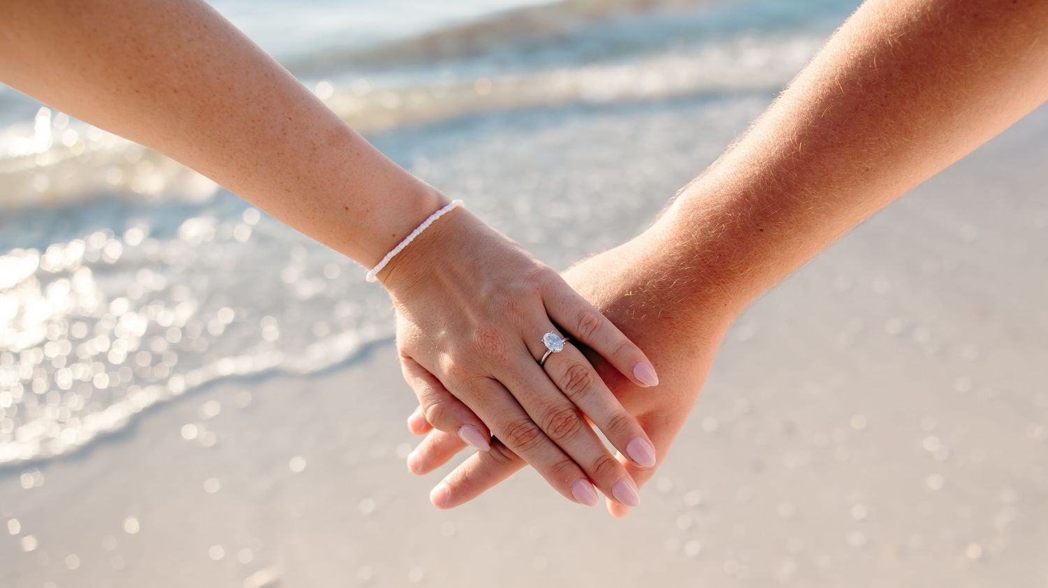 Hands gently playing with white sand on a beach as ocean waves roll in during sunset.