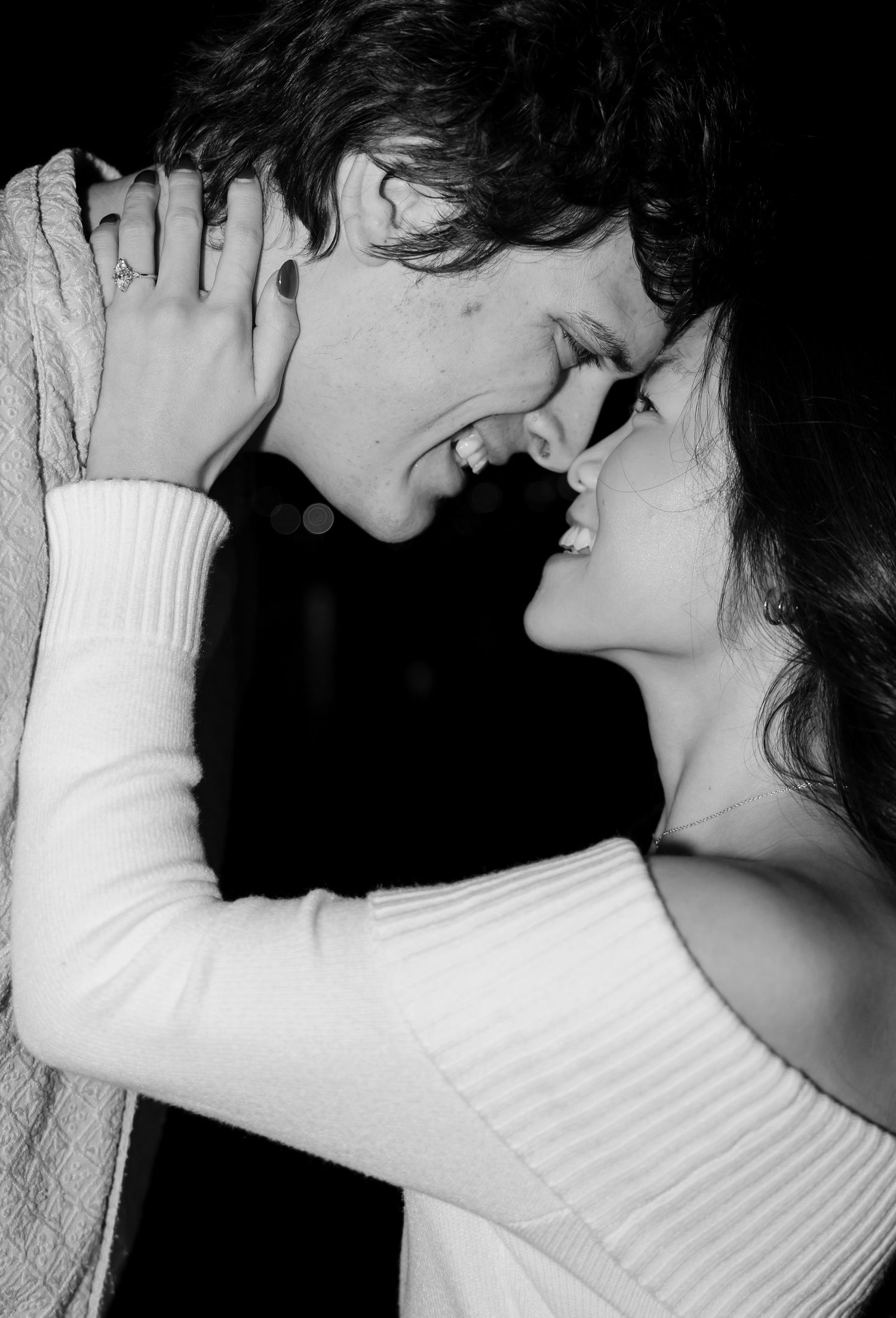 Black and white photo of a smiling couple sharing a romantic moment, faces close together in an embrace.