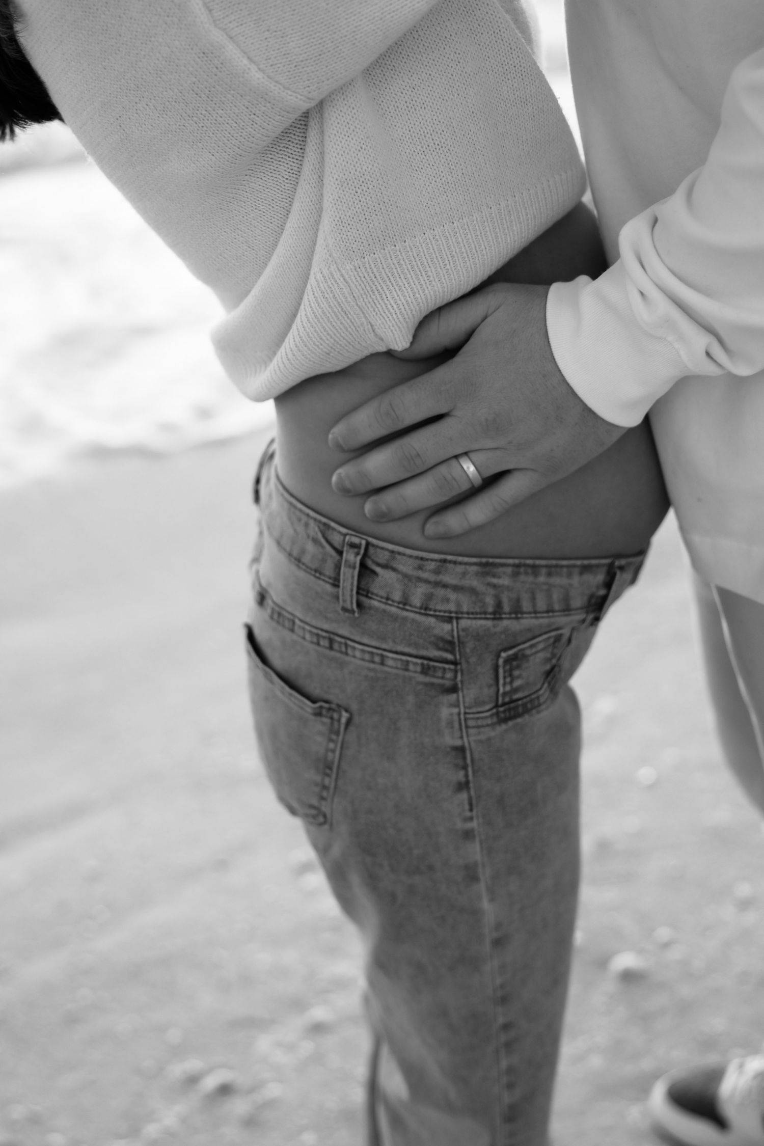 Black and white photo of a couple embracing, man's hand with wedding ring resting on woman's hip in jeans.