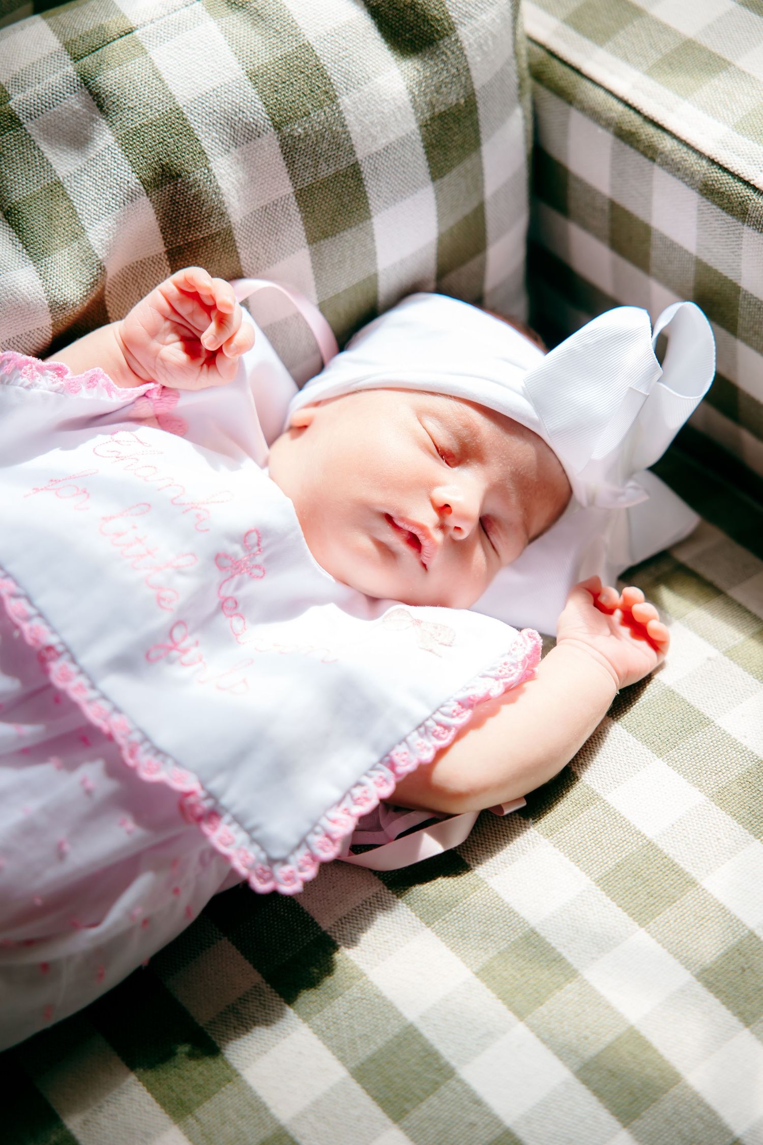 Newborn baby sleeping peacefully on plaid chair wearing pink outfit and white bunny hat.