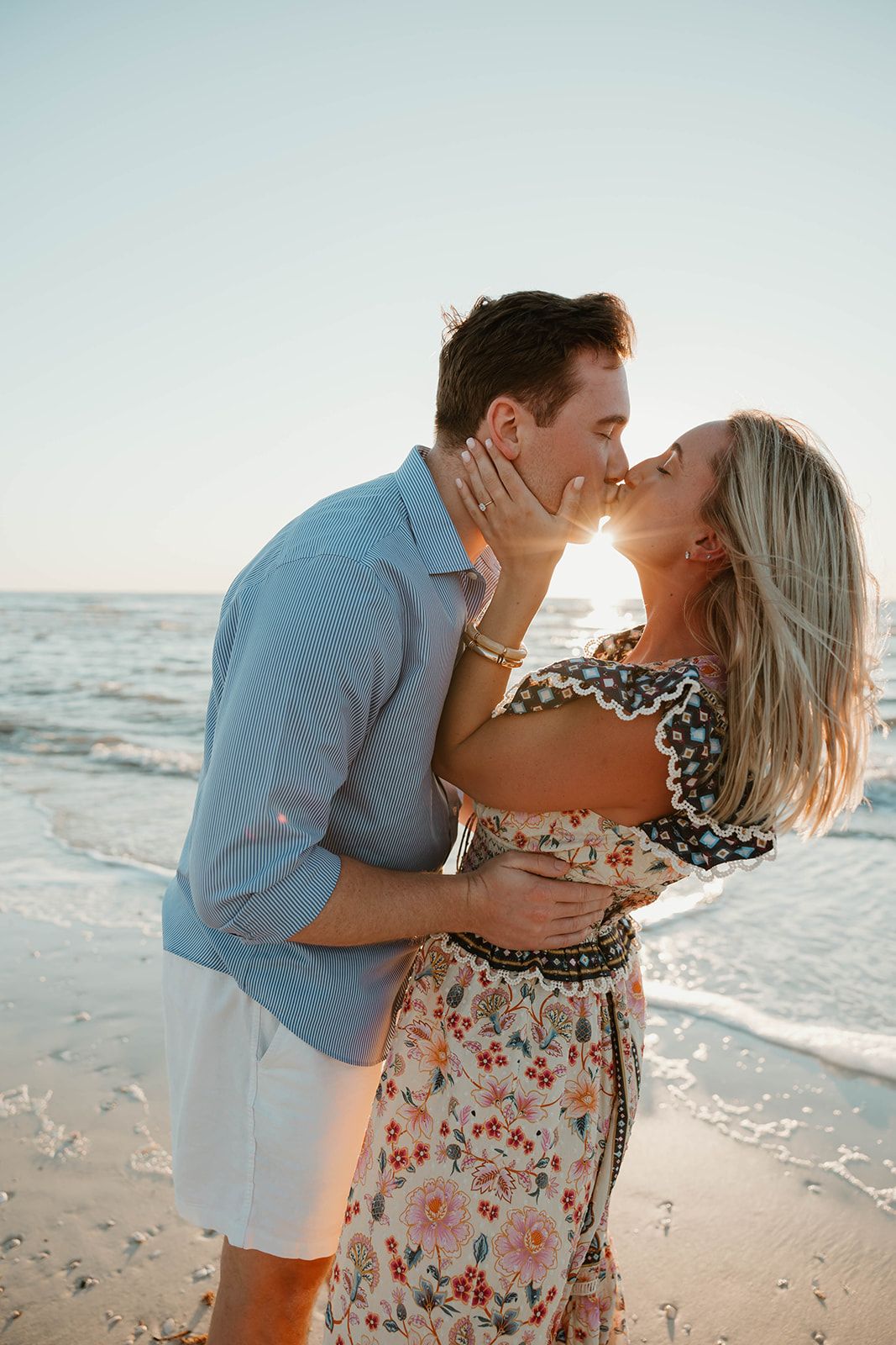 A romantic beachside kiss with ocean waves in the background during sunset.