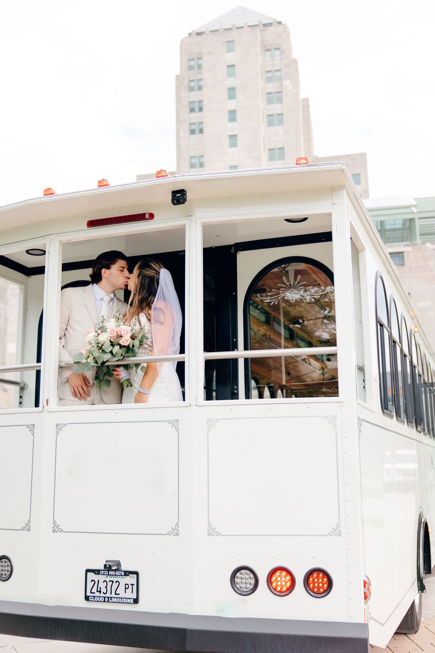 Bride and groom sharing a kiss on a white trolley bus on their wedding day in the city.