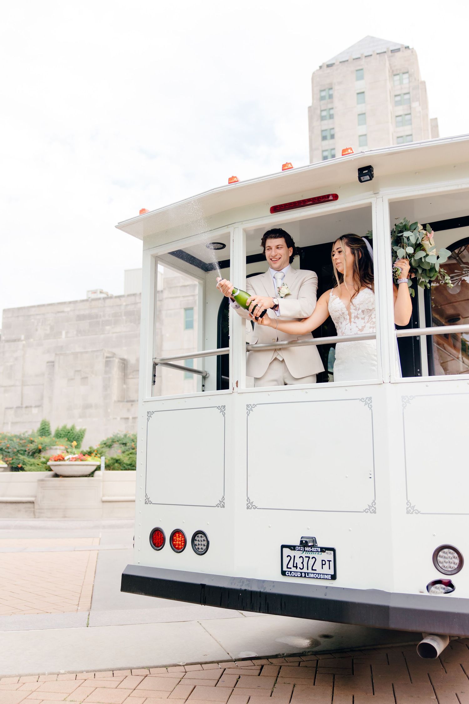 Bride and groom pop champagne on a white wedding trolley in the city.