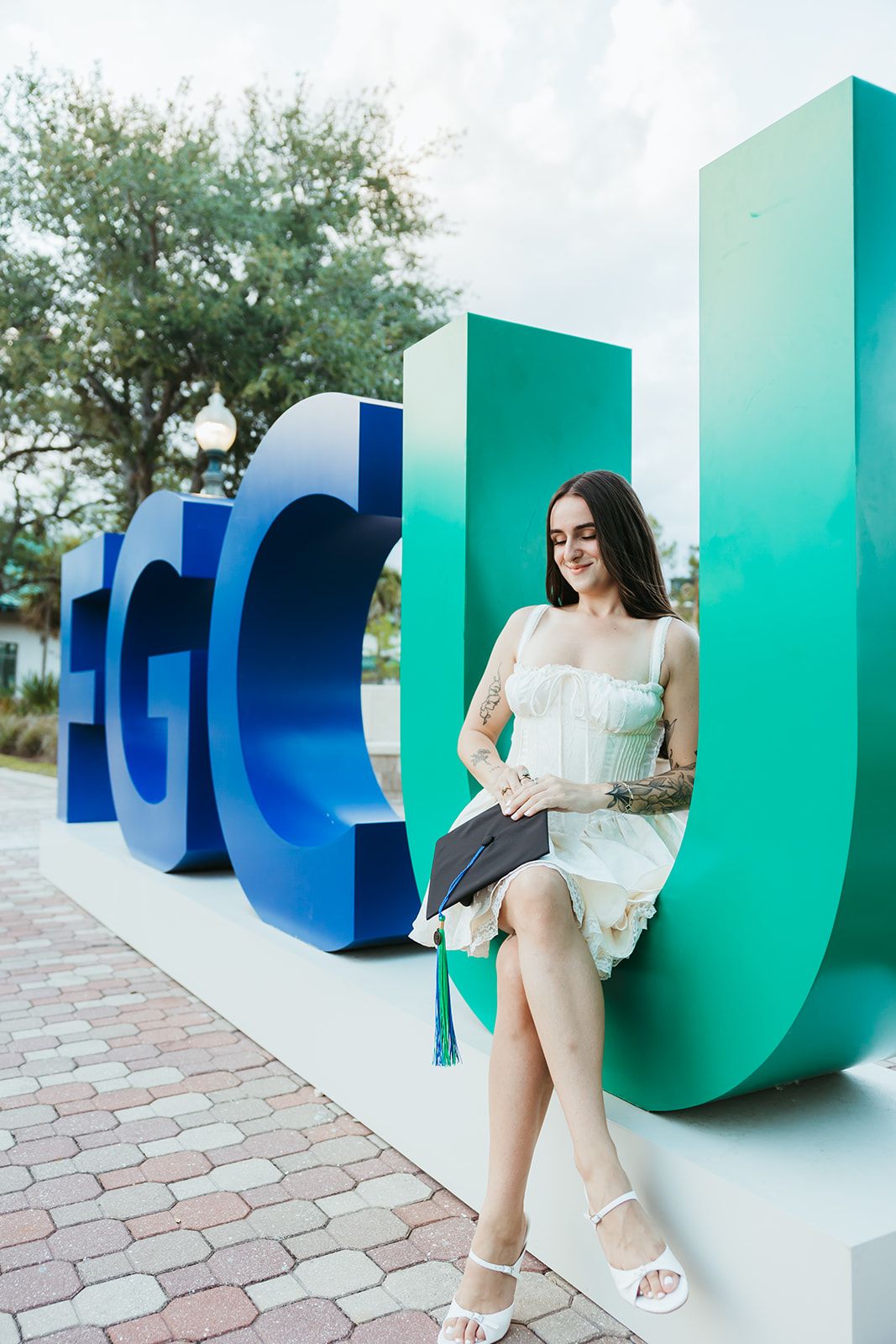A white dress and colorful geometric wall installation featuring turquoise and blue sculptural elements on brick pavement.