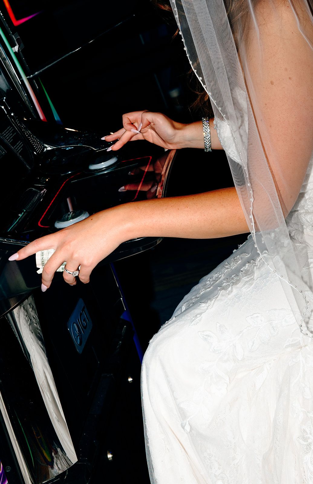 Bride in white wedding dress and veil playing slot machines at a casino on her wedding day.