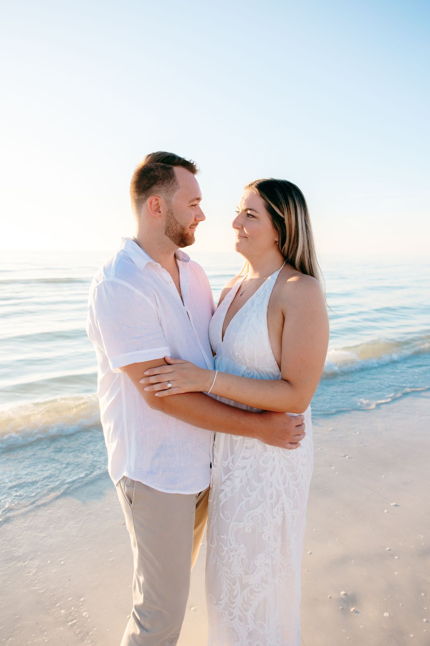 A couple shares a joyful moment together while embracing on a sunny beach with ocean waves in the background.