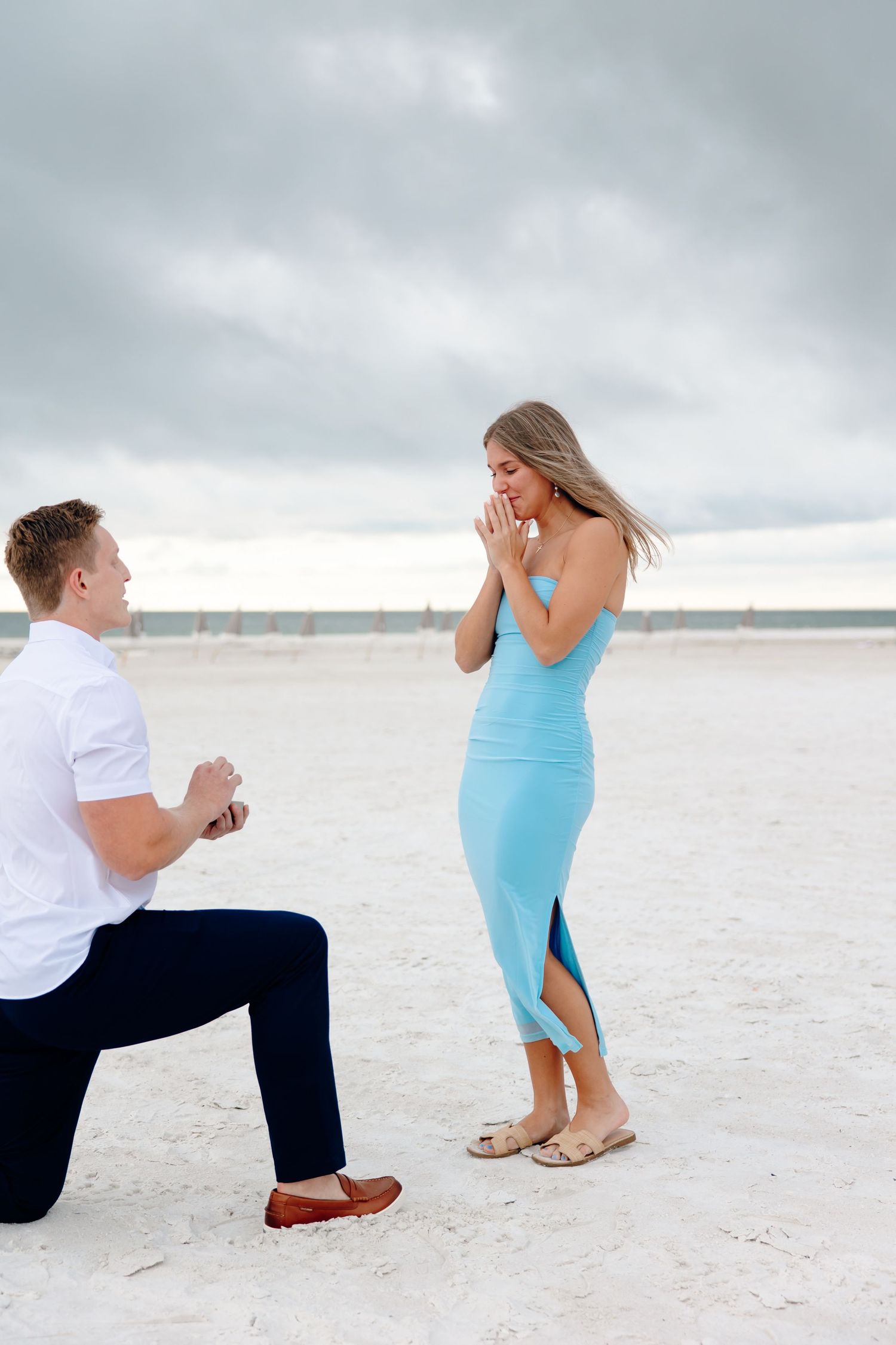 A marriage proposal sequence on a white sandy beach with cloudy skies showing a couple in blue and white attire.