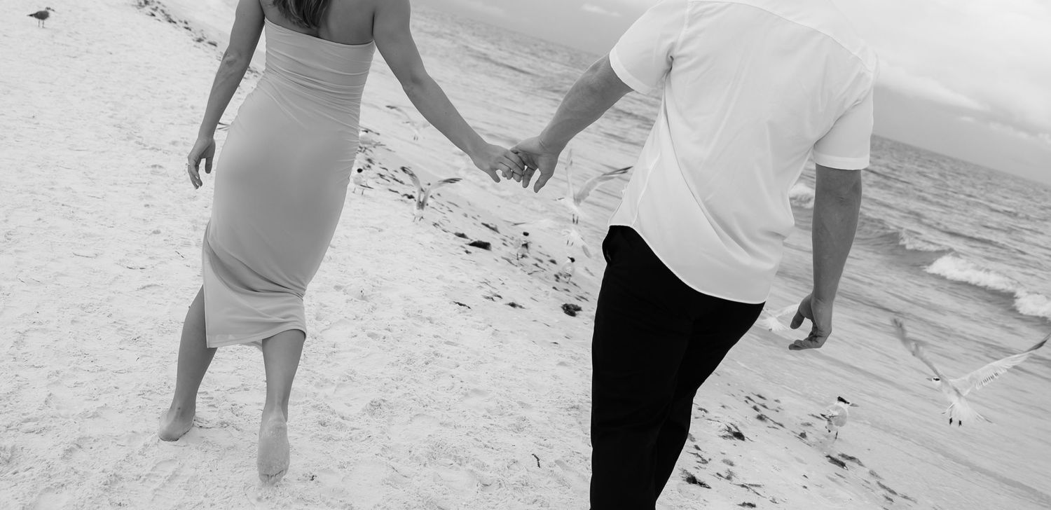 A person wearing white walks along a sandy beach near the ocean waves at sunset.