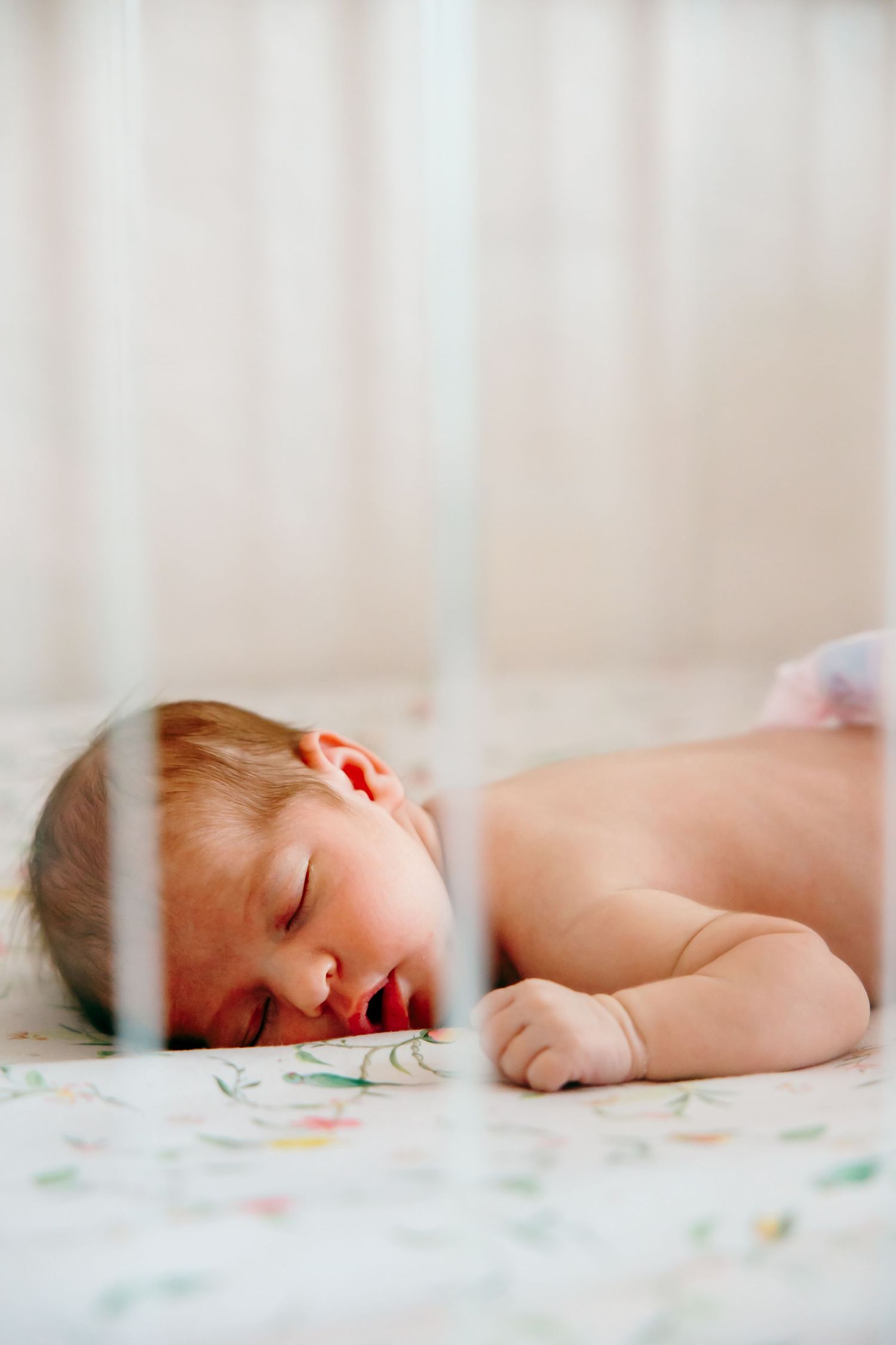Newborn baby sleeping peacefully on its stomach in a white crib with floral bedding.