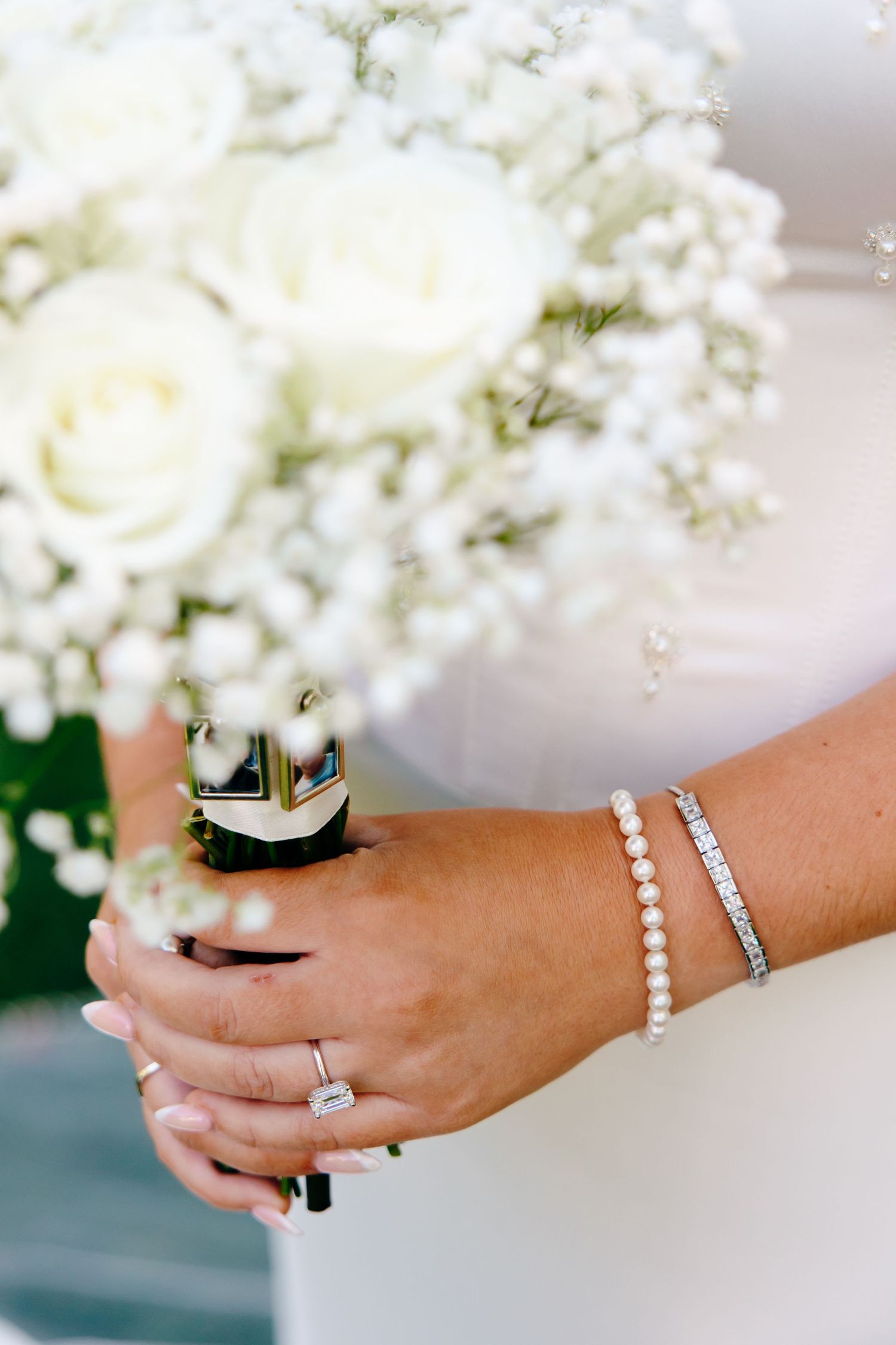 A delicate pearl bracelet and diamond wedding band adorn a wrist against a backdrop of white hydrangea flowers.