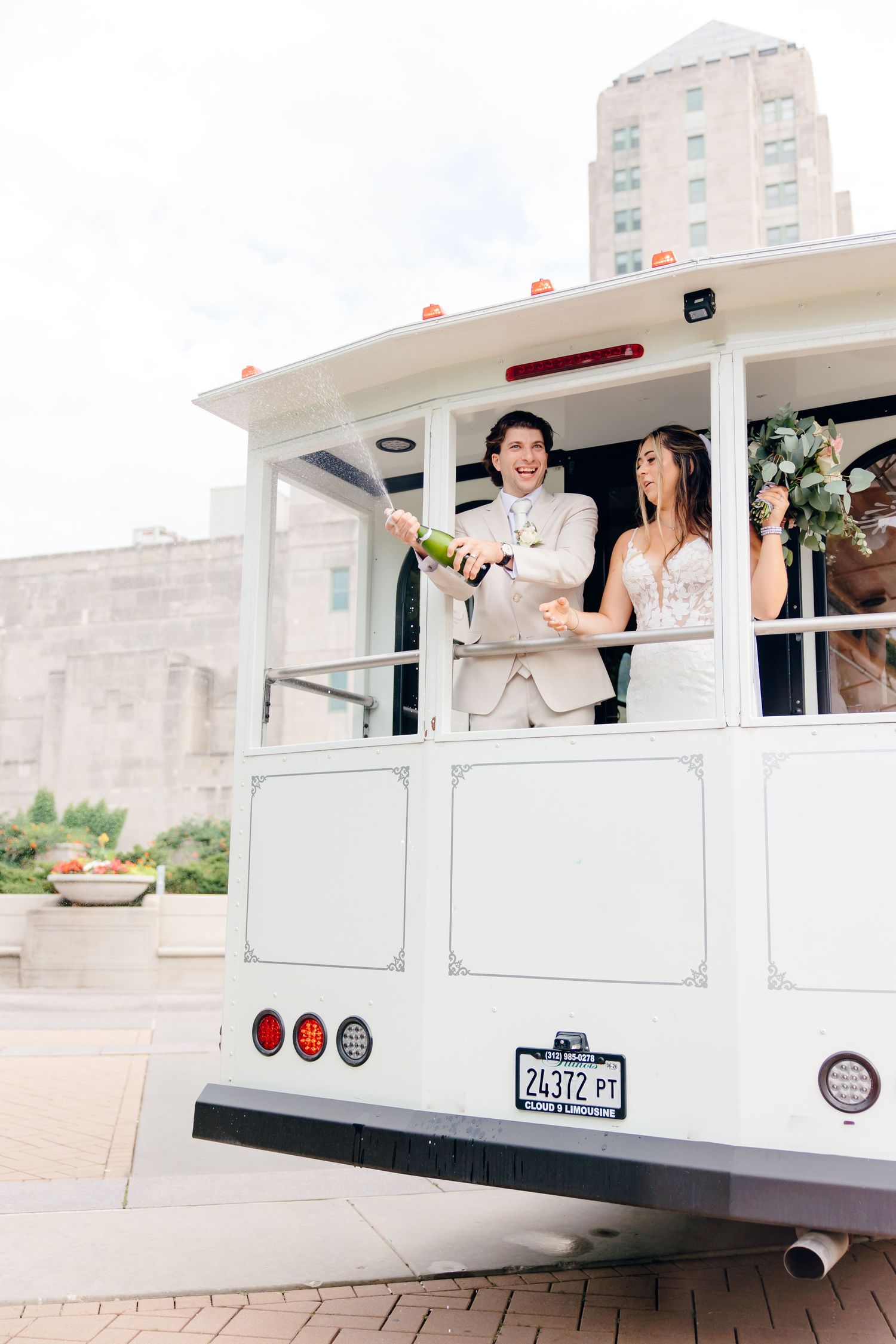 Bride and groom popping champagne on a white trolley car on their wedding day.