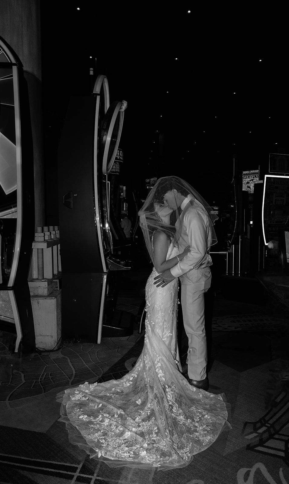 Black and white photo of a bride and groom sharing a romantic kiss, her lace gown and veil trailing elegantly.