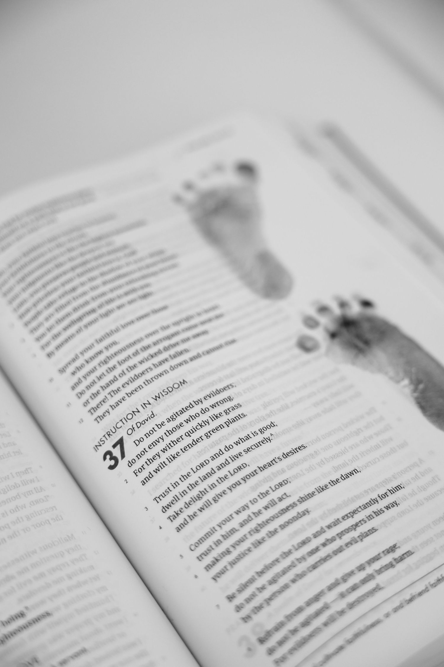 Open Bible displaying Psalm 37 with two baby footprints in black and white, symbolizing faith and new life.