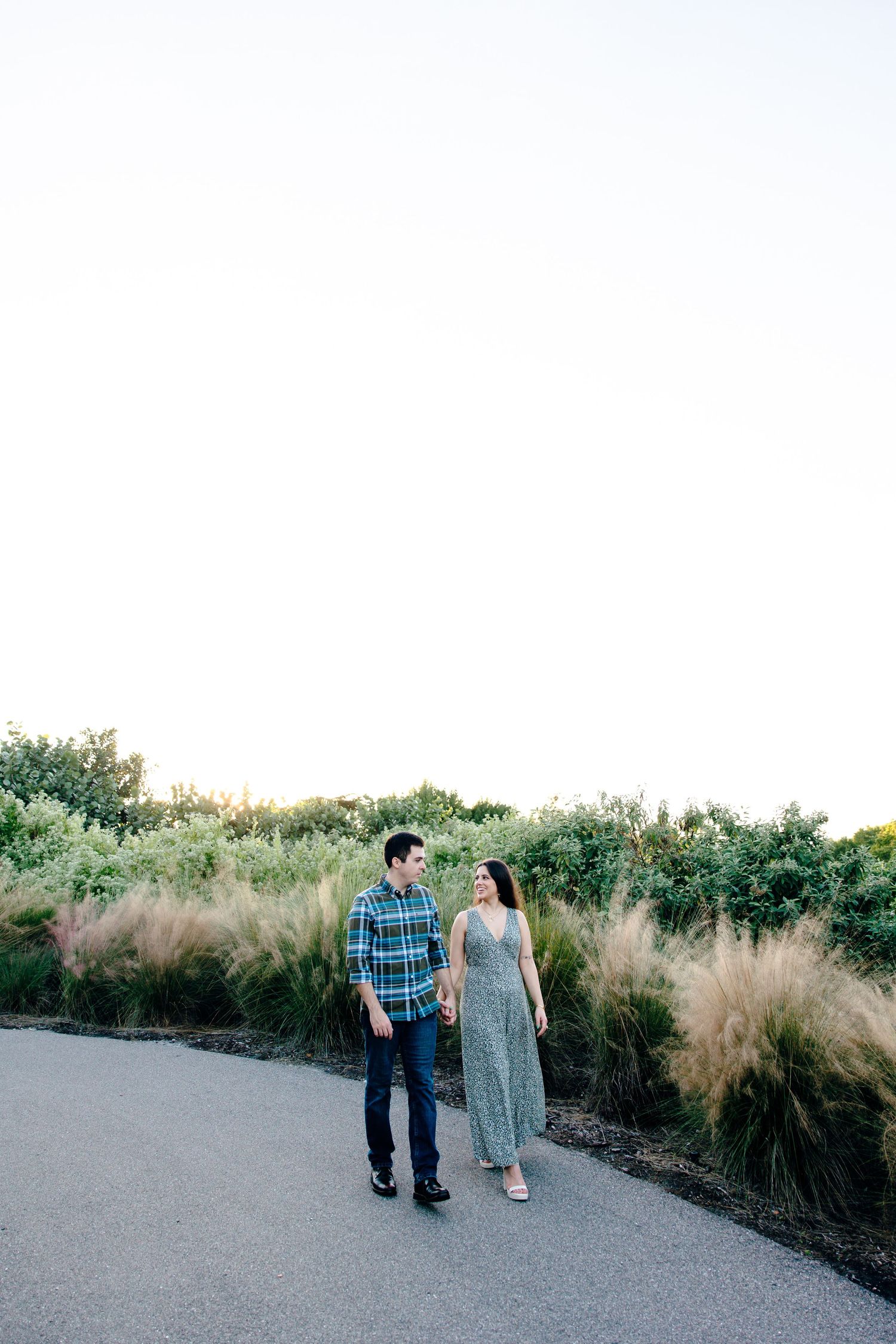 Couple walking hand in hand on a path surrounded by lush greenery during golden hour.