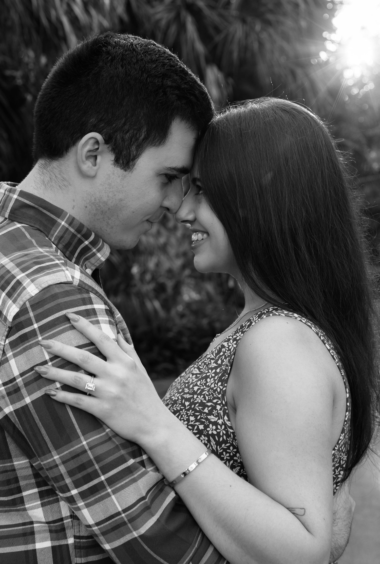 Black and white photo of a smiling couple leaning foreheads together outdoors, woman wearing bracelet and ring.