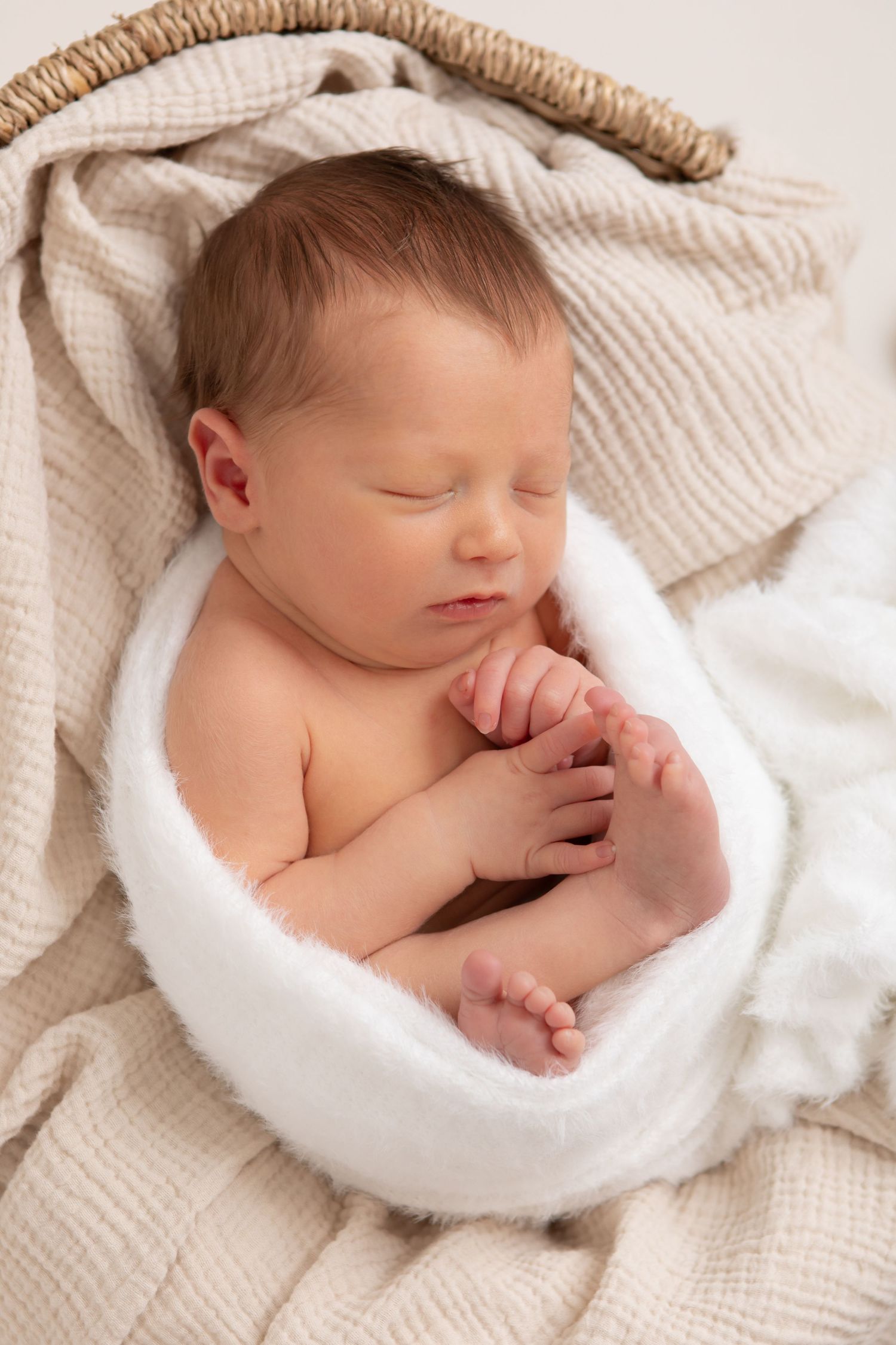 Sleeping newborn curled up in soft white blankets with delicate lighting.