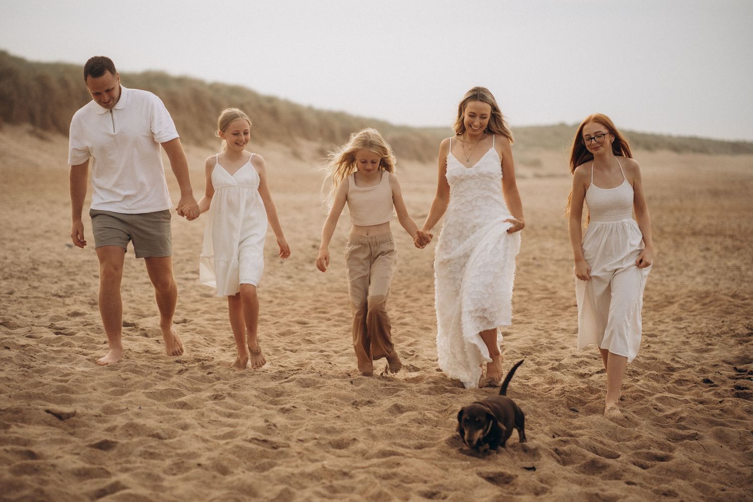 Family walking together on sandy beach during golden hour.