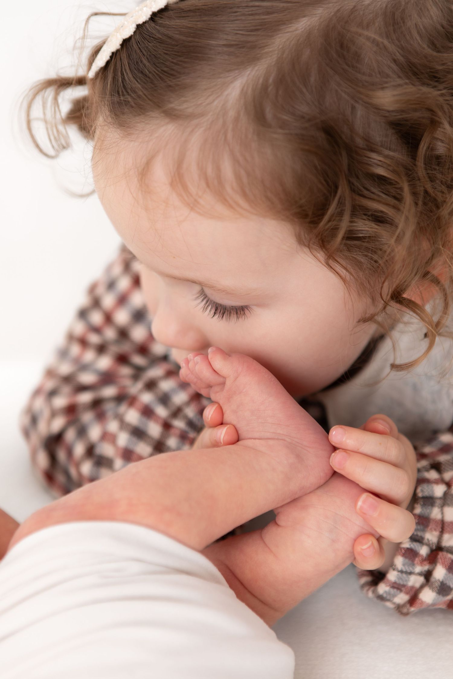 Sweet moment captured as toddler in checkered shirt kisses baby sibling.