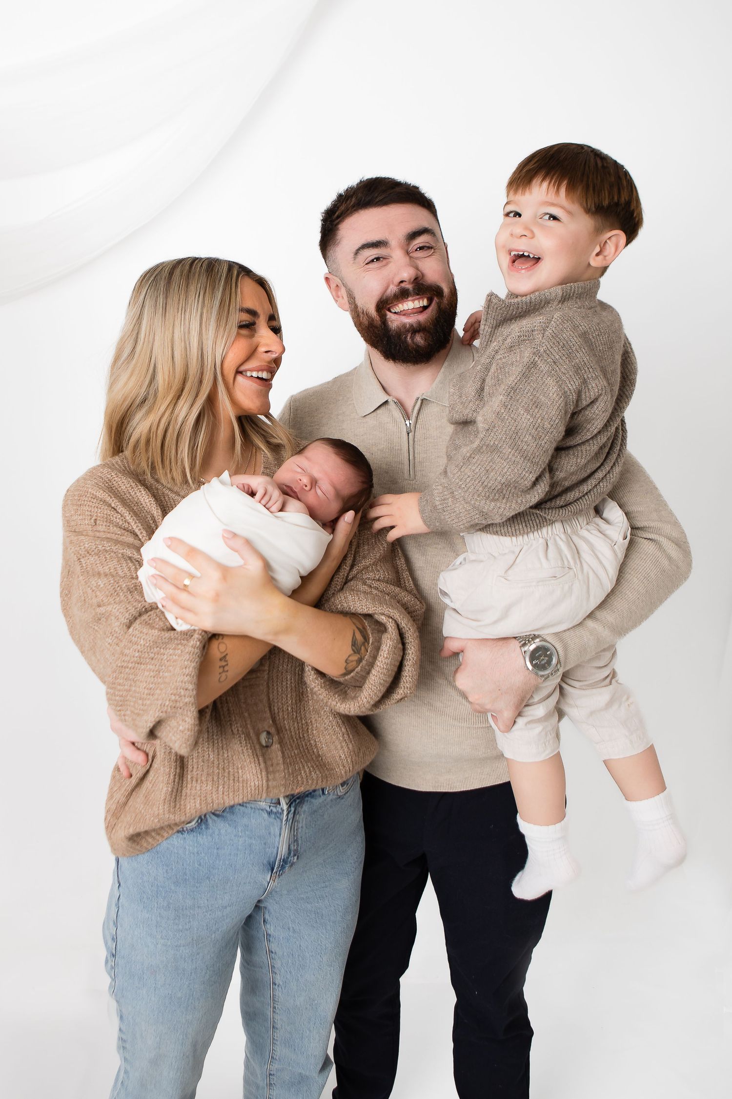Family wearing neutral tones shares joyful moments in studio photography.