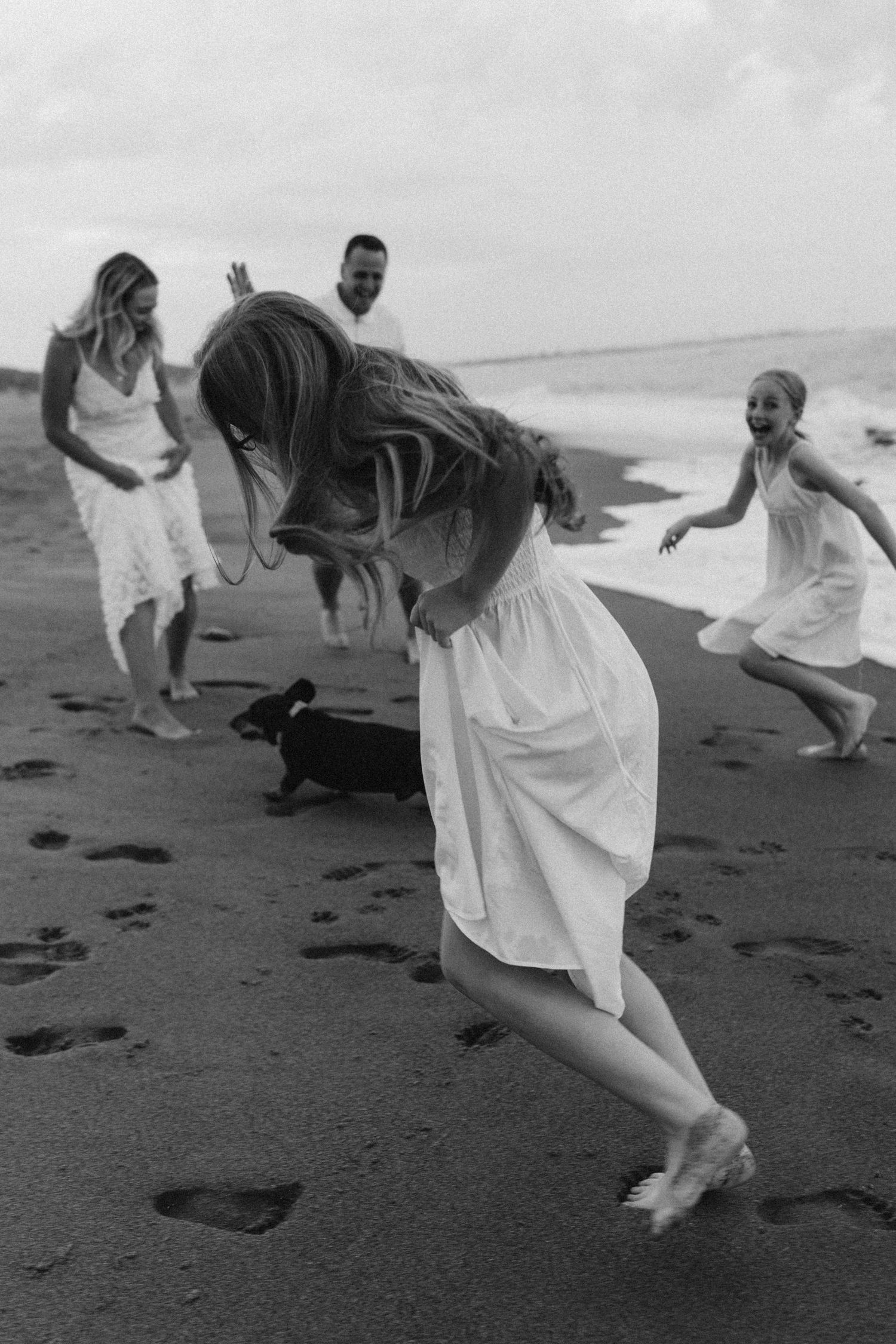 A playful family moment on the beach with a small dog running in black and white.