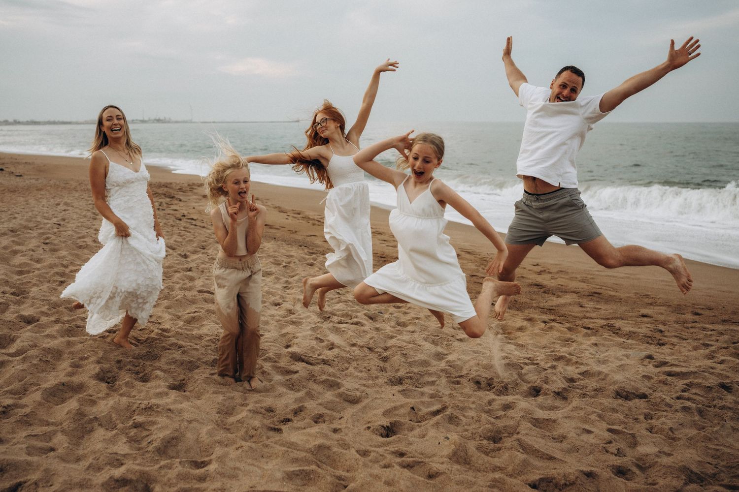 Group jumping and playing together on beach with arms raised in celebration.